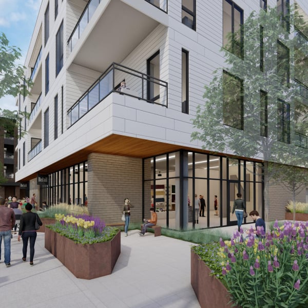 Modern apartment building with large windows, balconies, plants, and people walking and sitting outside.