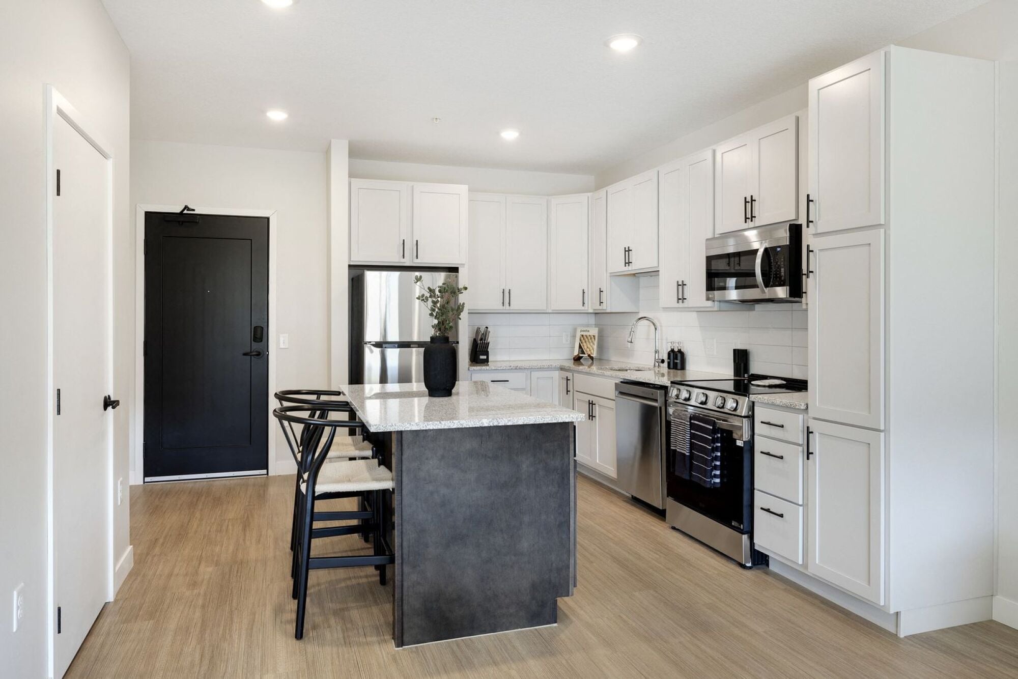 A modern kitchen with a black door and white cabinets.