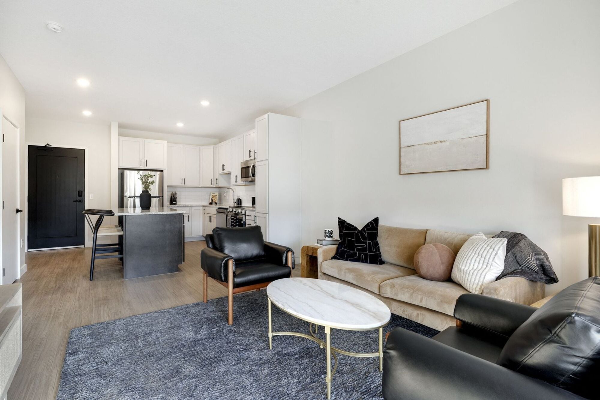 A living room with a black leather couch, a white coffee table, and a grey rug at The Blakeley in Shakopee, MN.