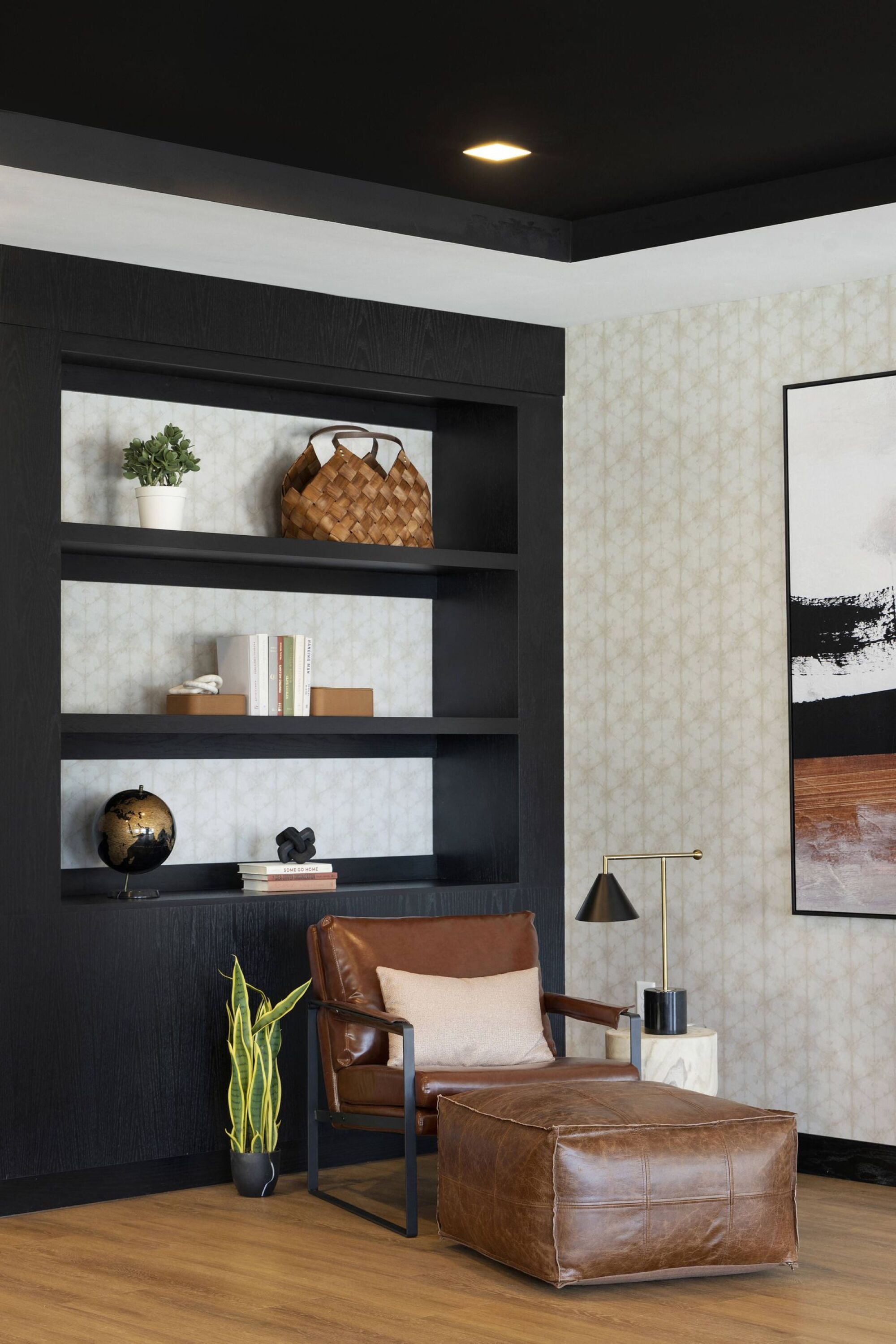 A brown leather chair sits in front of a shelf with a plant and a globe on it.
