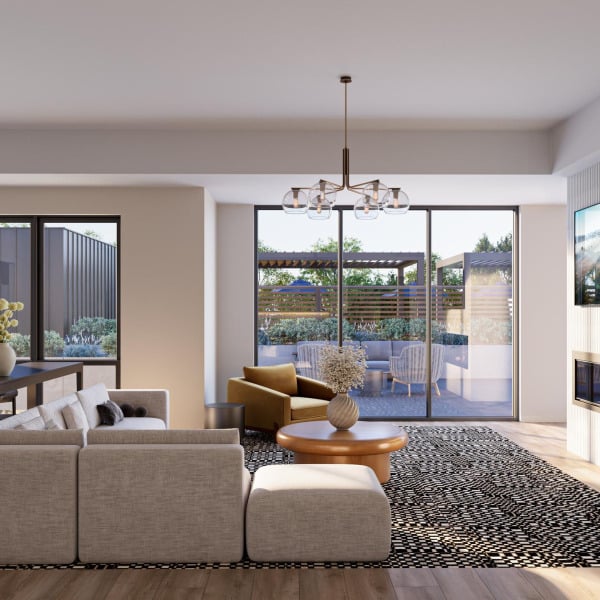 Modern clubroom with light beige sofa, round coffee table, and glass doors opening to a sunny patio with seating.