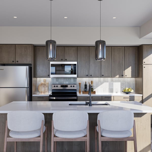 Modern kitchen with gray cabinets, a stainless steel fridge and stove, and three white chairs at an island.