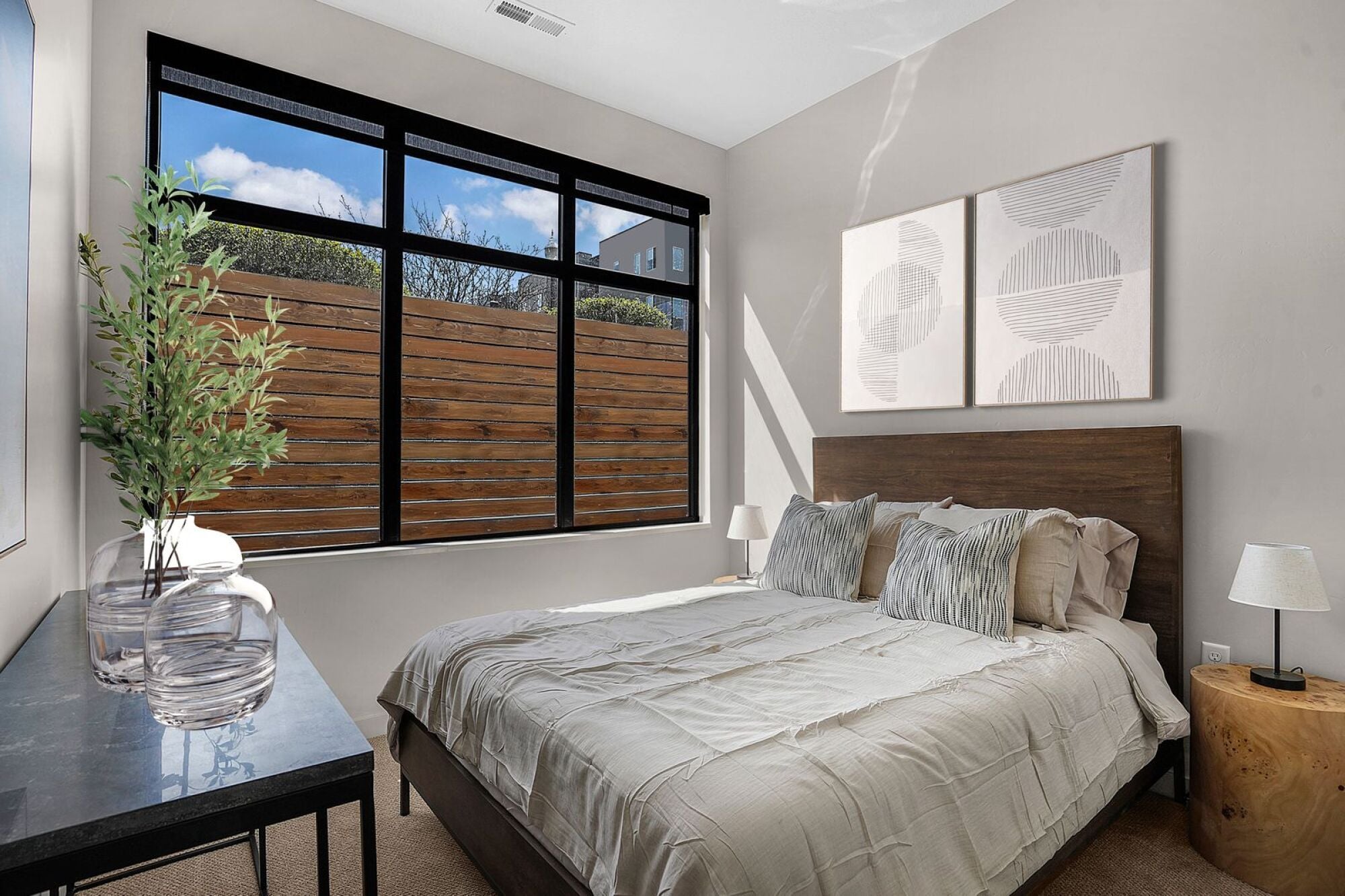 A bedroom with a large bed, a table with a vase and a potted plant, and two framed artworks on the wall at The Whitney in Salt Lake City, Utah.