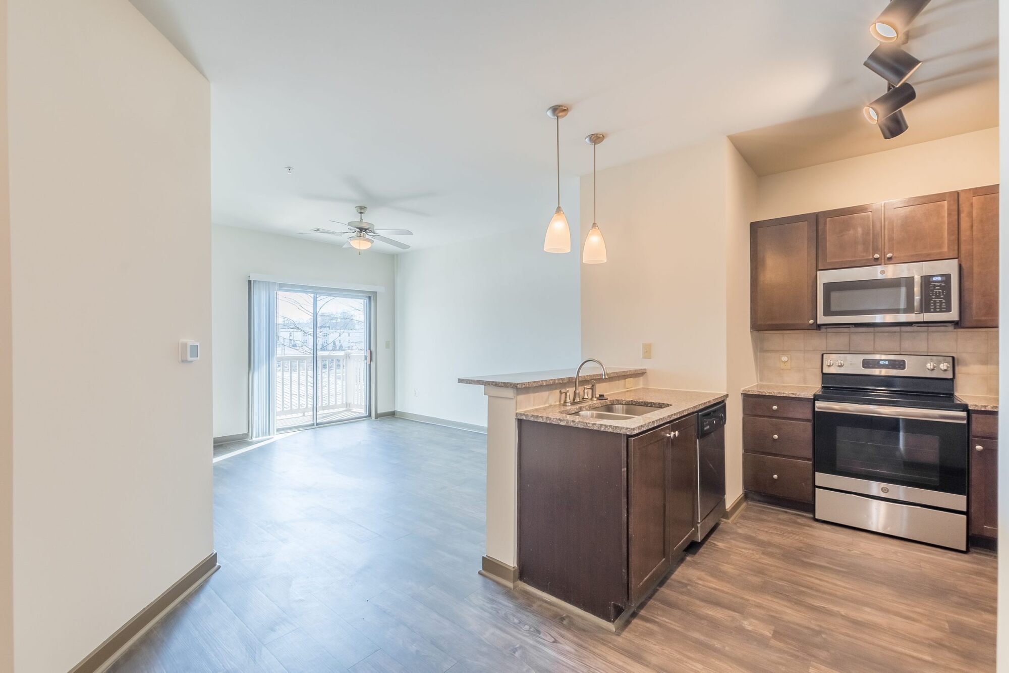 Modern kitchen with dark cabinets, pendant lights, and open living area with sliding glass doors to a balcony.