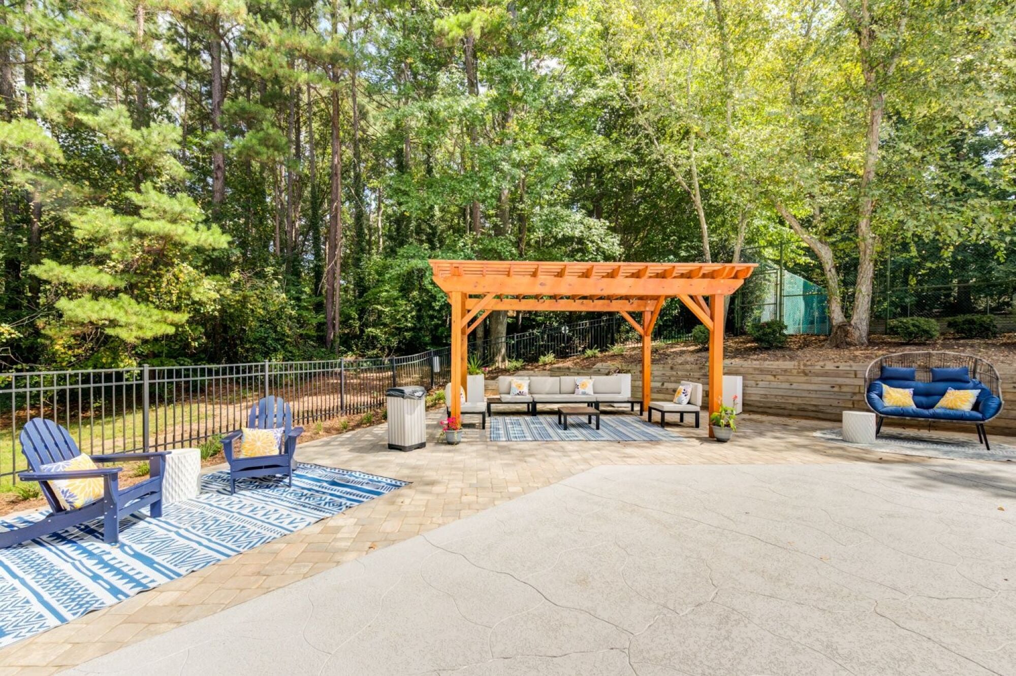 A wooden pergola is in the middle of a concrete patio with chairs at Laurel Oaks in Raleigh, NC.
