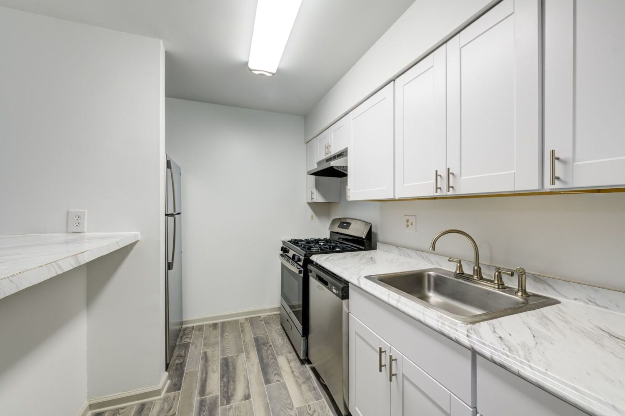 A renovated kitchen with a white refrigerator, a stove, a dishwasher, and a sink.
