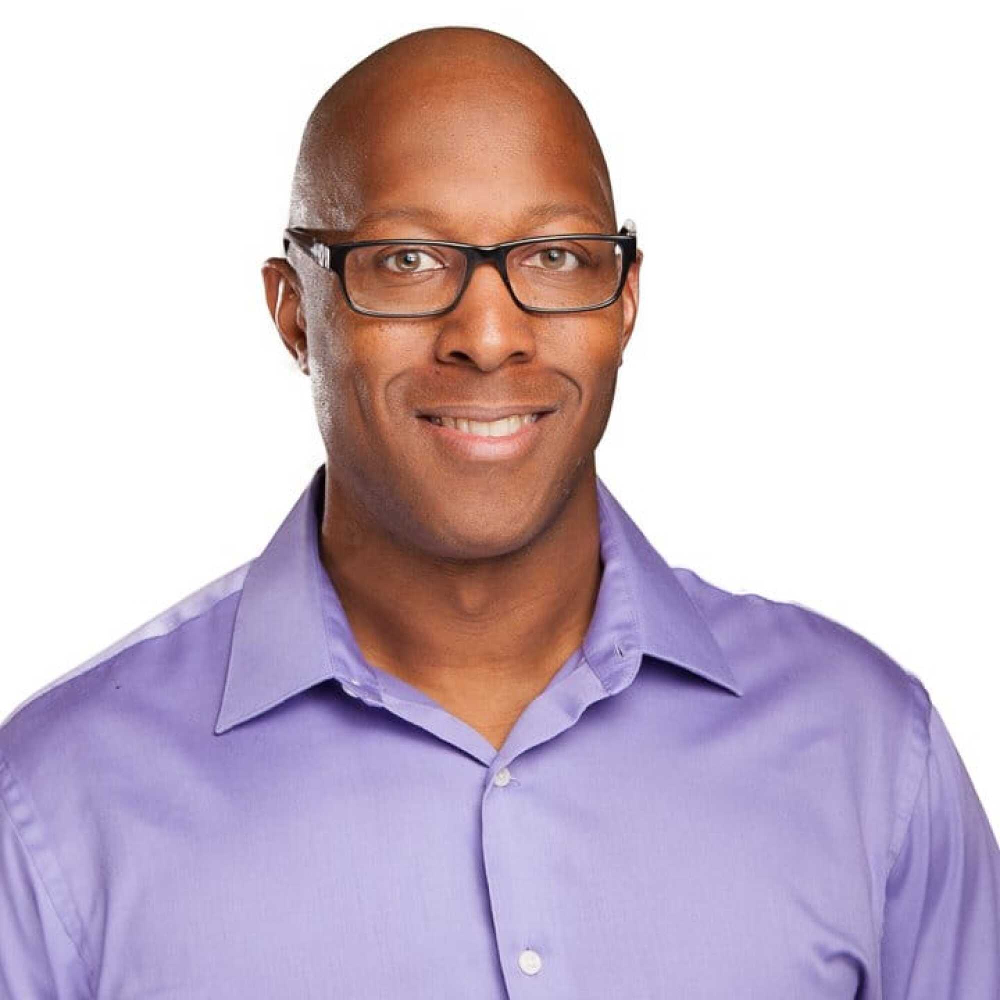 Man in a blue Venterra shirt sits at a desk, smiling, with a white wall and paper holder in the background.