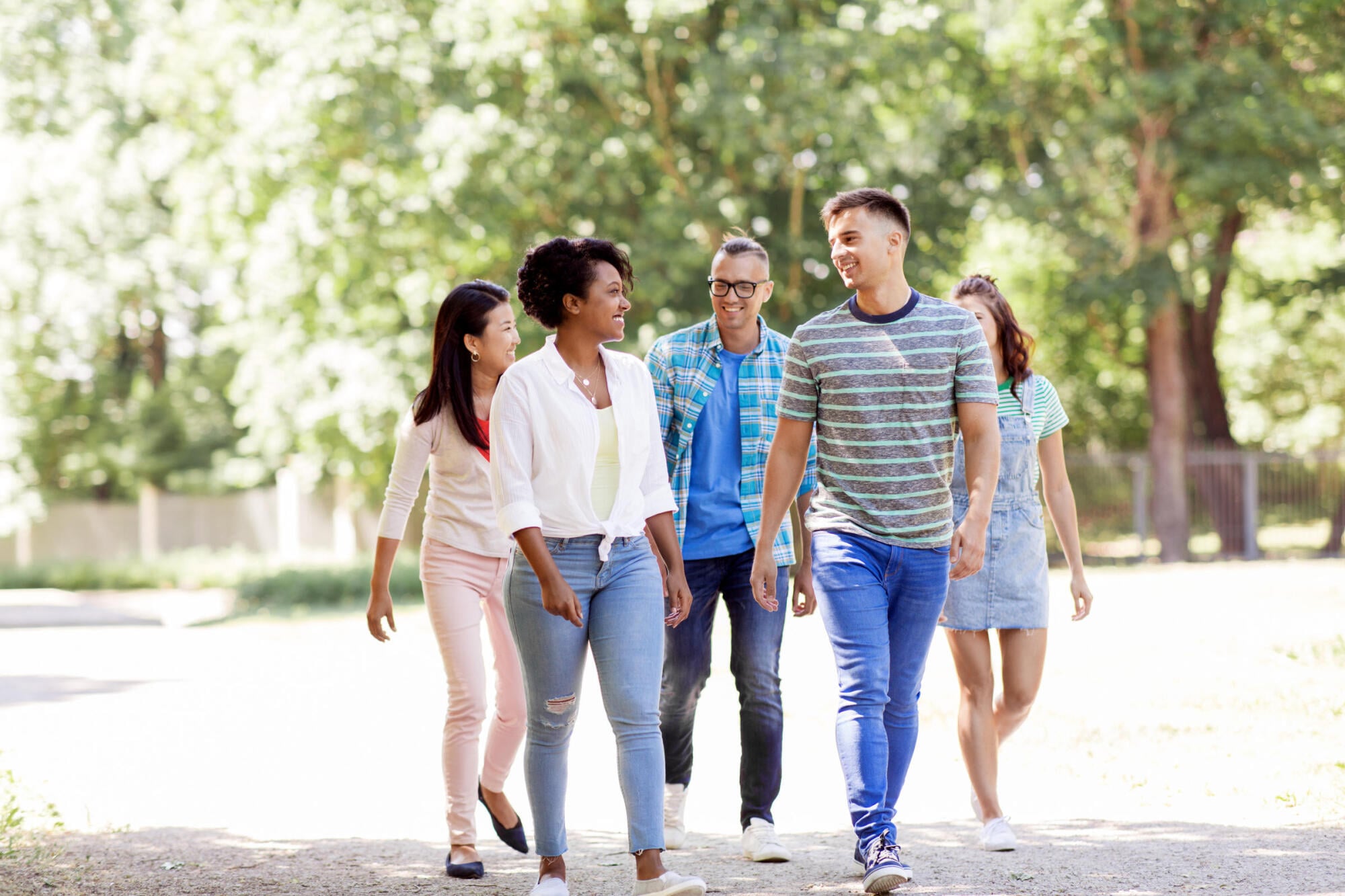 Group of college friends walking and laughing together along a tree-lined path on a sunny day.