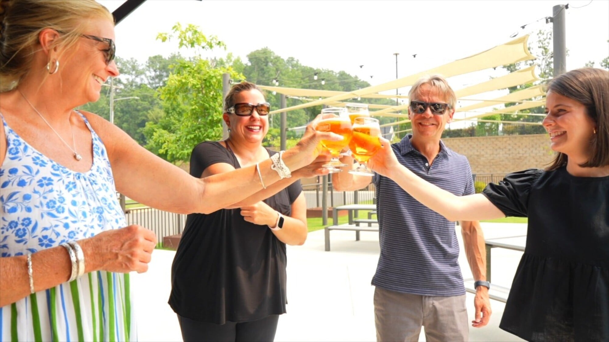 Four people clink glasses of beer at an outdoor brewery.