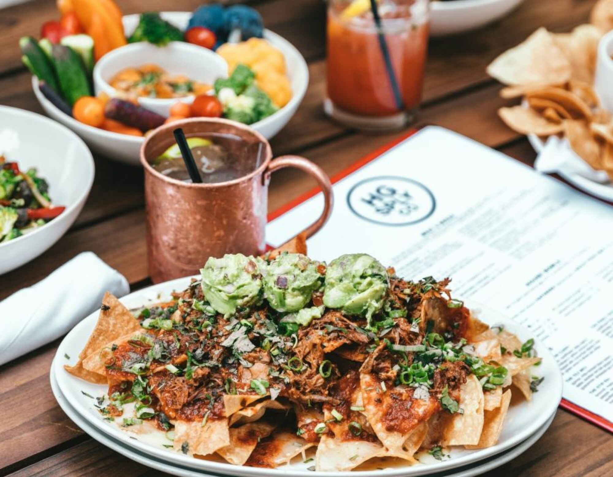 Sonder A plate of nachos with melted cheese, accompanied by chips and a bowl of salsa, set on a rustic wooden table.