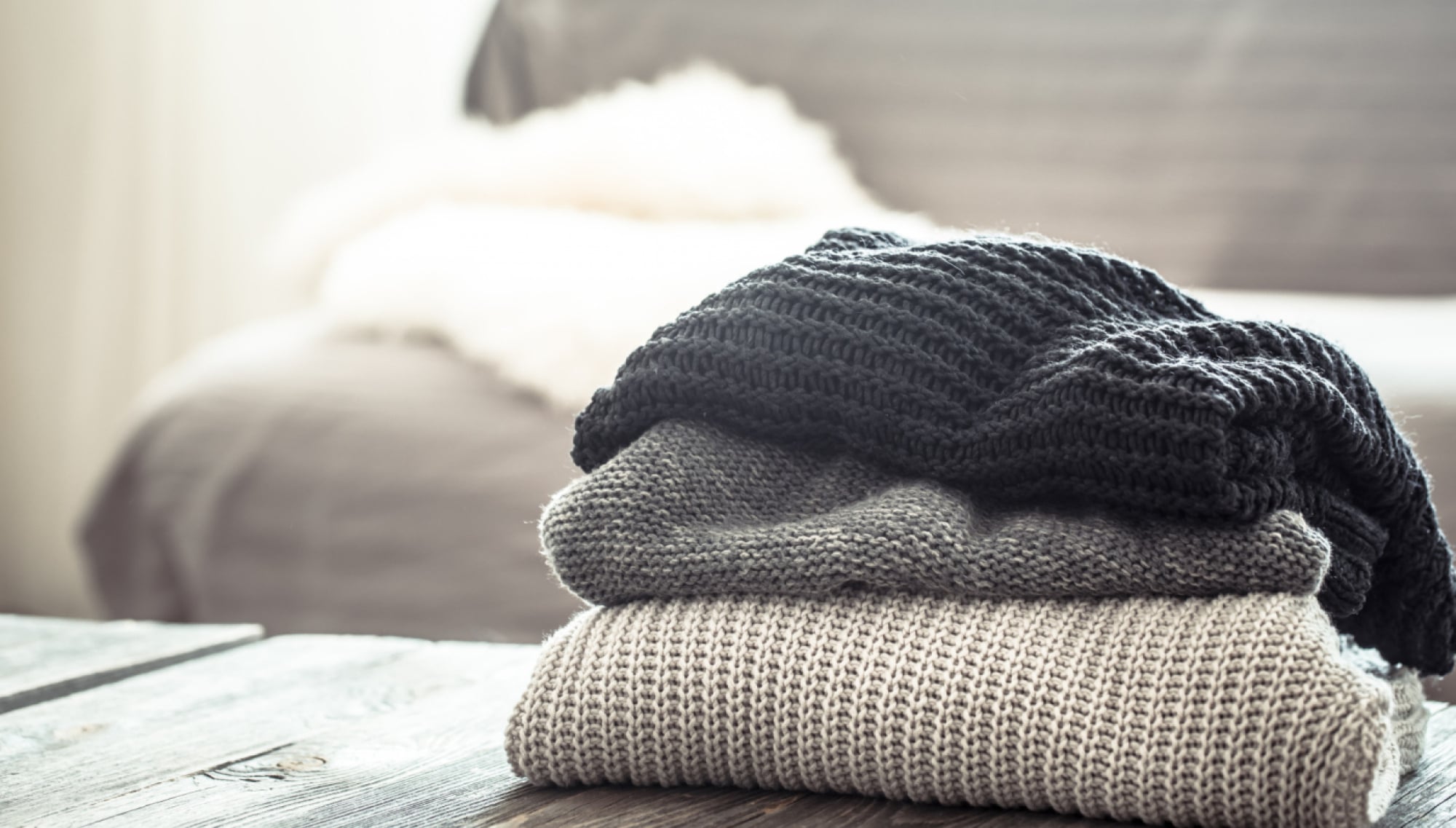 The Wade Three colorful sweaters neatly stacked on top of each other, showcasing different textures and styles.