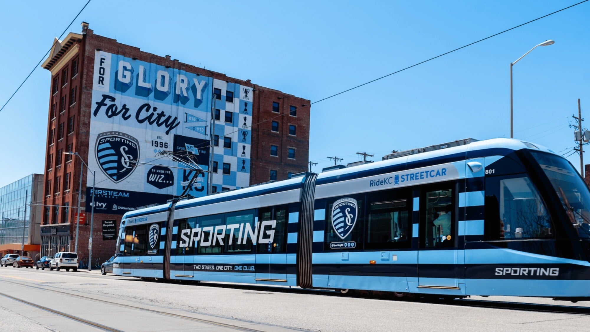 The Wade A blue and white tram travels along a city street, surrounded by buildings and trees.