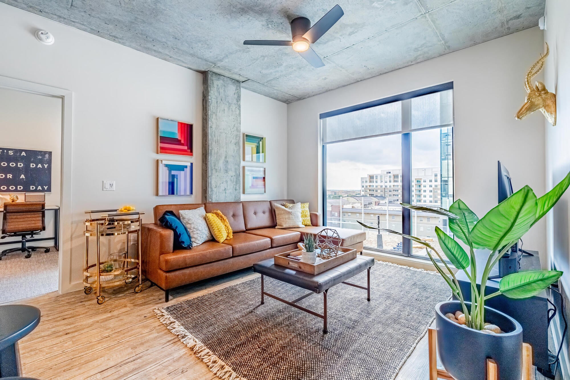 Furnished living room with floor-to-ceiling windows and city views at Rev in College Station, TX.