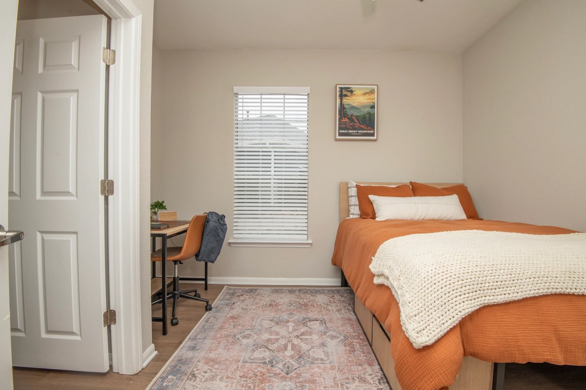 Furnished bedroom at The Heights with orange bedding, a desk, and window.