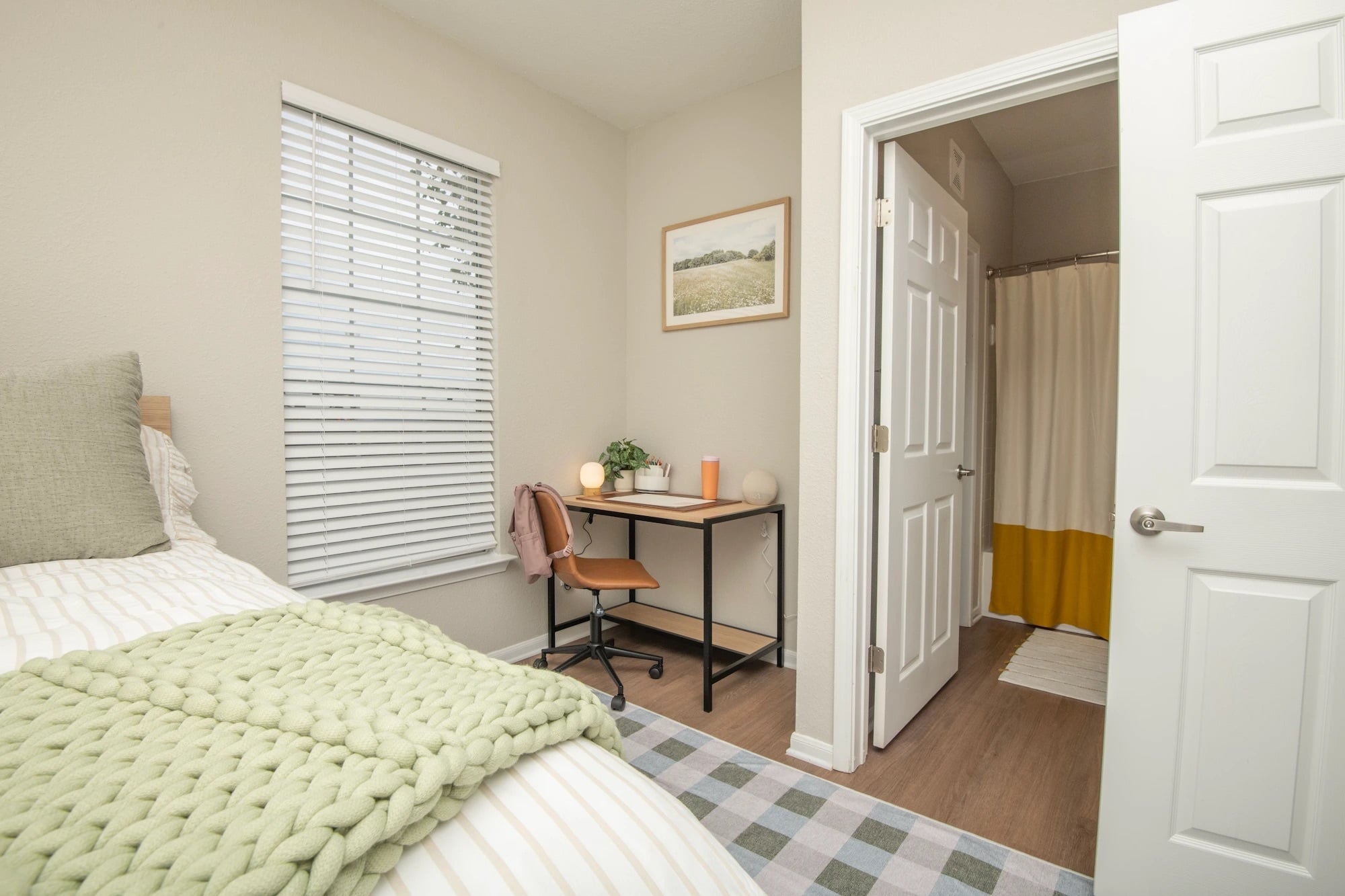 Furnished bedroom at The Heights with a desk, green bedding, and an attached bathroom.