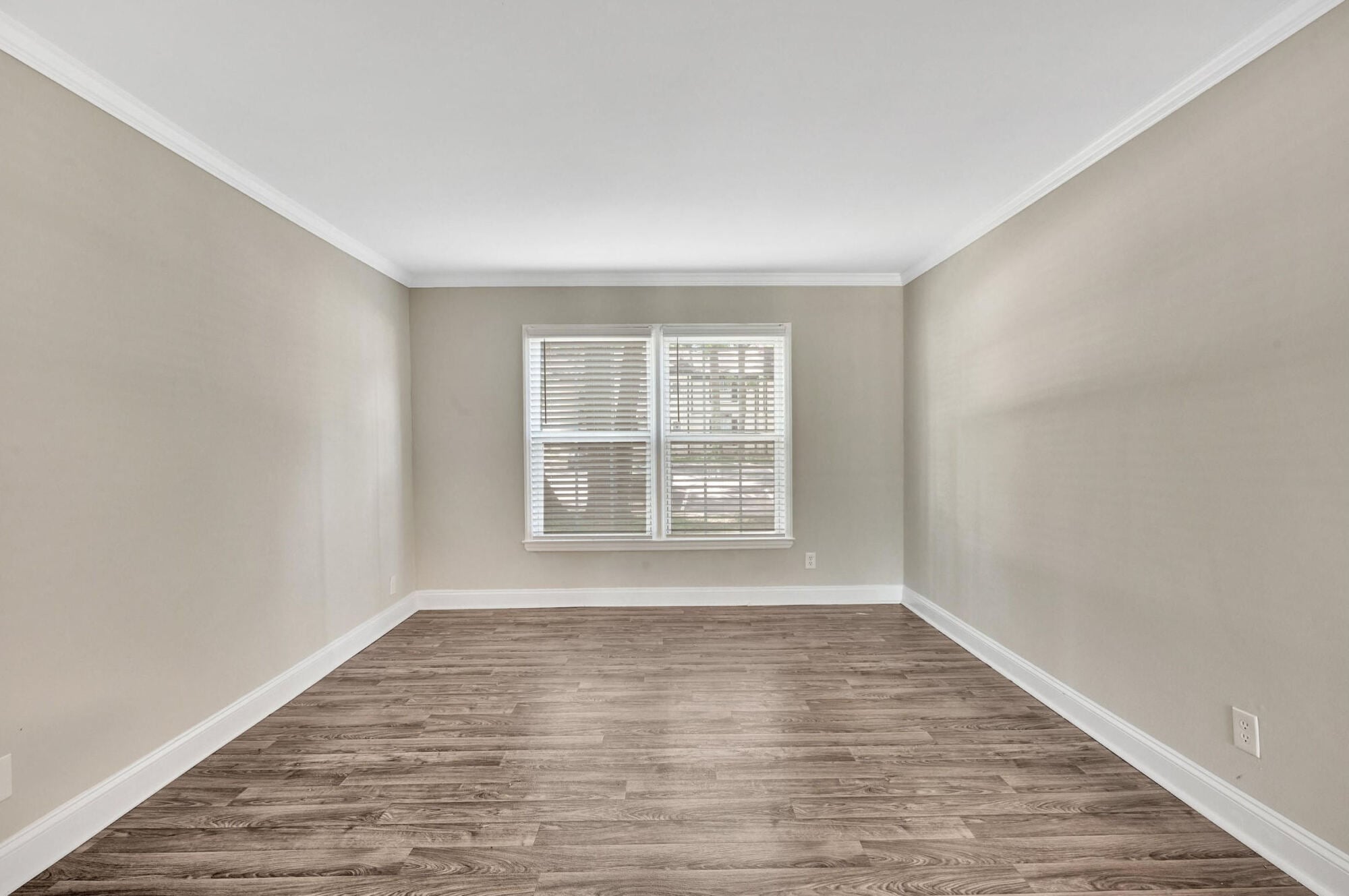 Bright bedroom at Maple Run in Charlotte, NC featuring wood-style plank flooring, crown molding, and a large window.