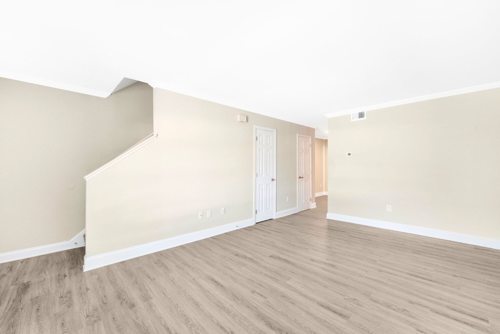 Empty room with light wood flooring, beige walls, white trim, and a staircase to the left leading upward.