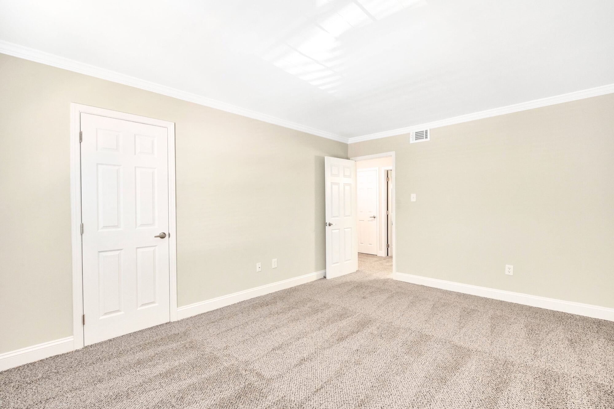 Empty room with beige walls, white trim, carpeted floor, and two white doors, one open to a hallway.