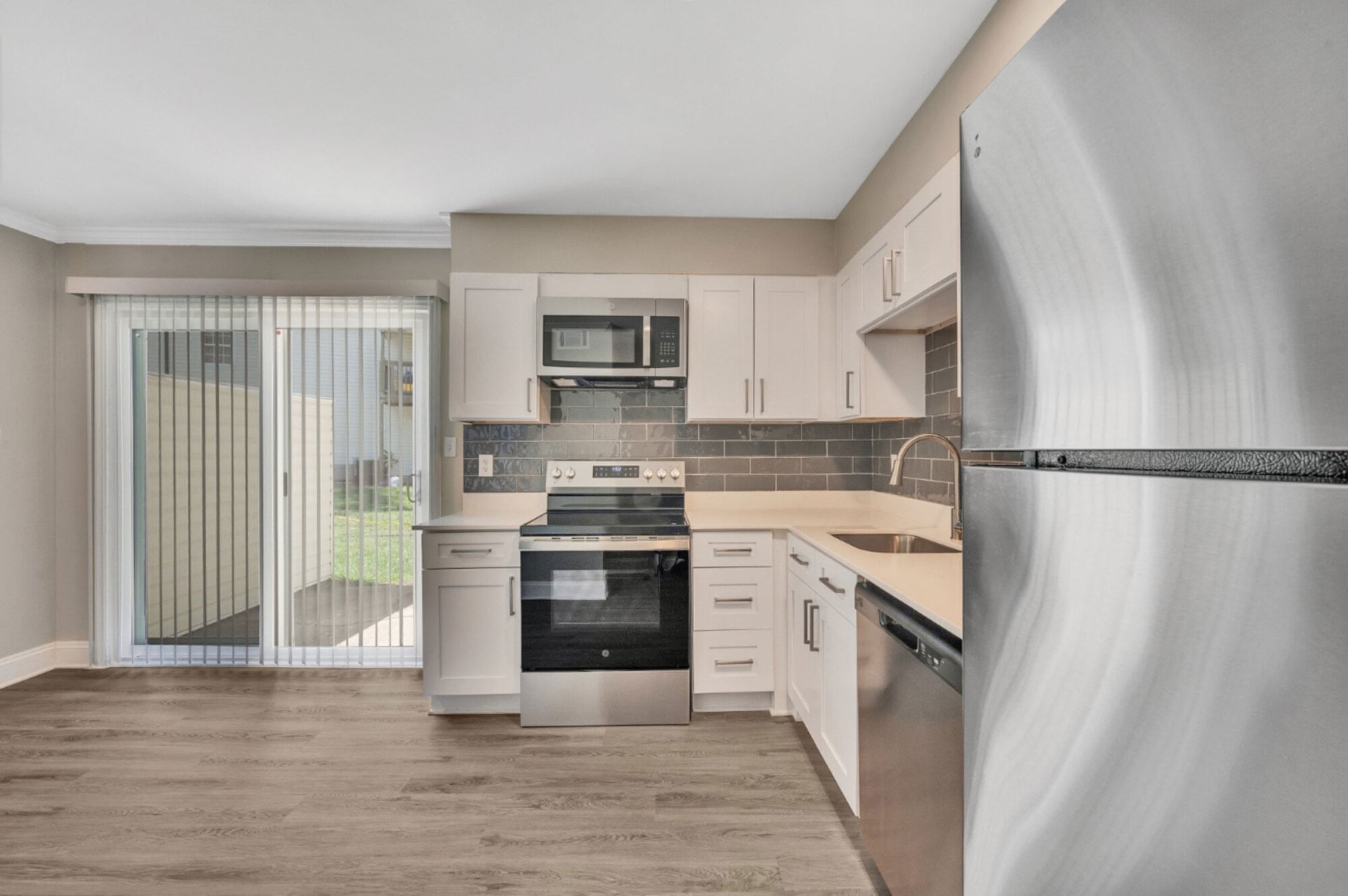 Modern kitchen with stainless steel appliances, white cabinets, tile backsplash, and sliding glass door to outside.