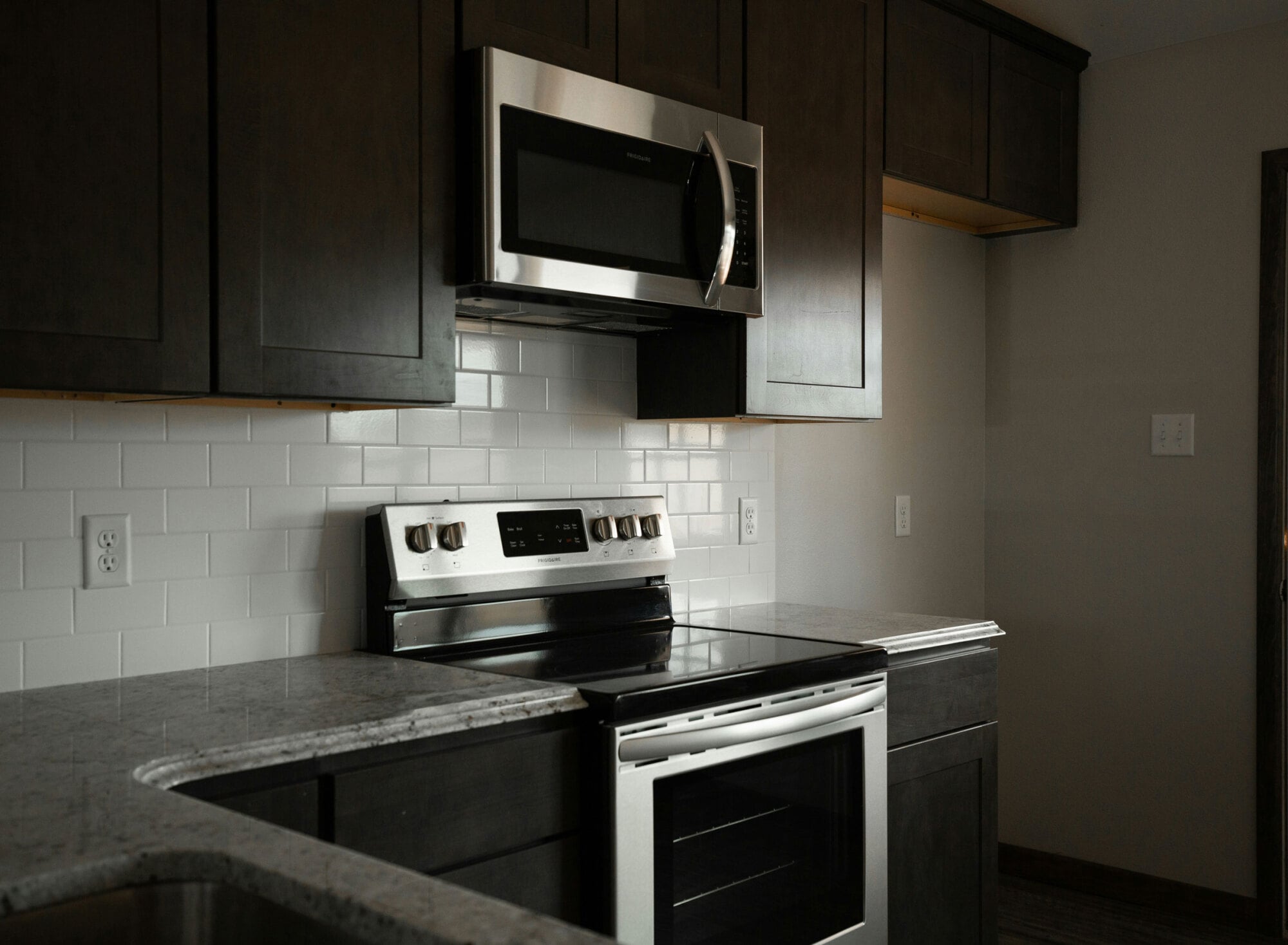 Modern kitchen with dark cabinets, white subway tile backsplash, stainless steel oven, and matching microwave above the stove.