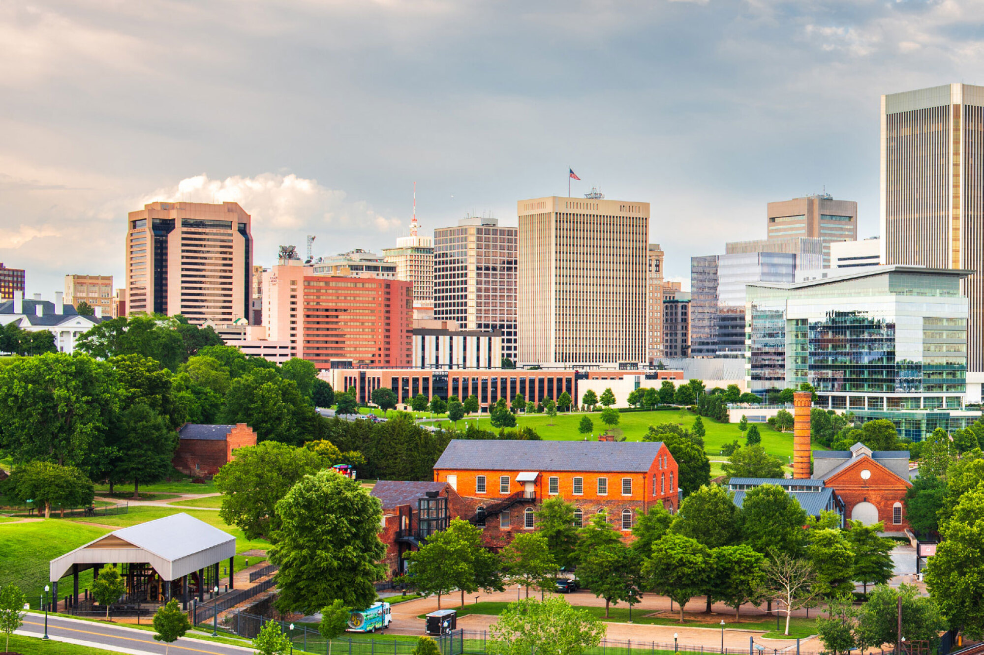 Skyline view of a city with tall modern buildings, green trees, and historic brick buildings in the foreground.