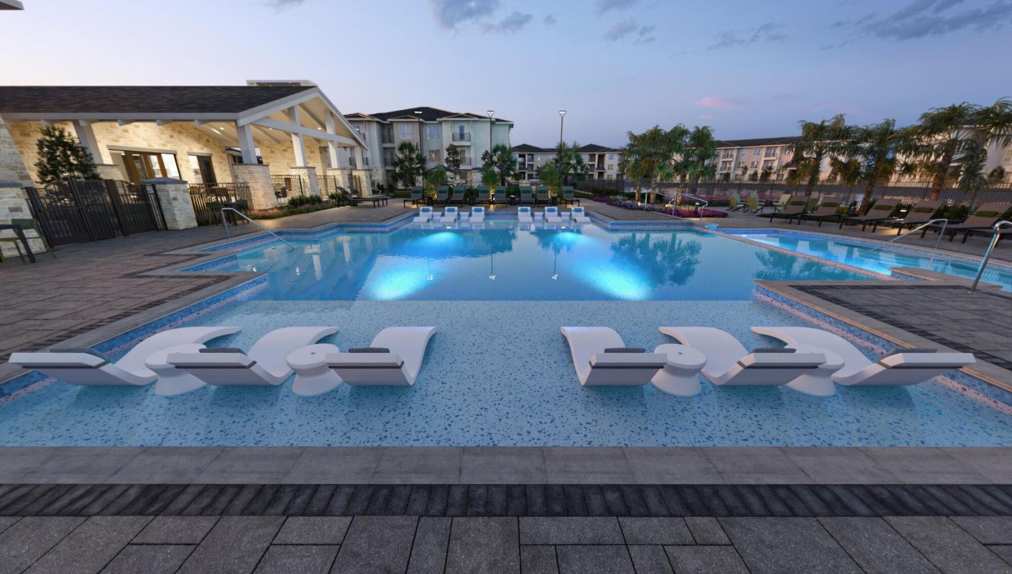 A large swimming pool with submerged lounge chairs, surrounded by apartment buildings at dusk.