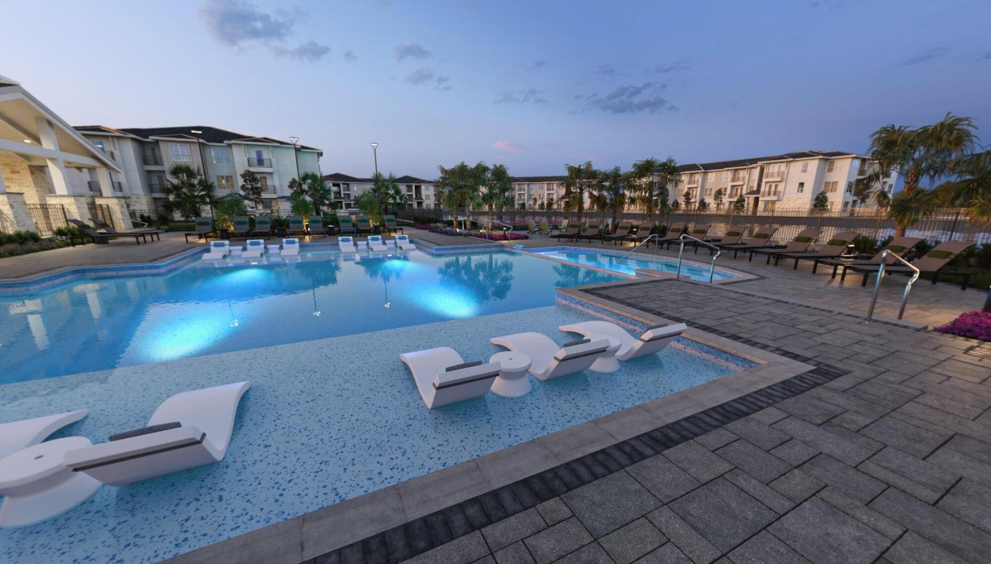 Modern outdoor pool at dusk, with lounge chairs in the water and apartment buildings in the background.