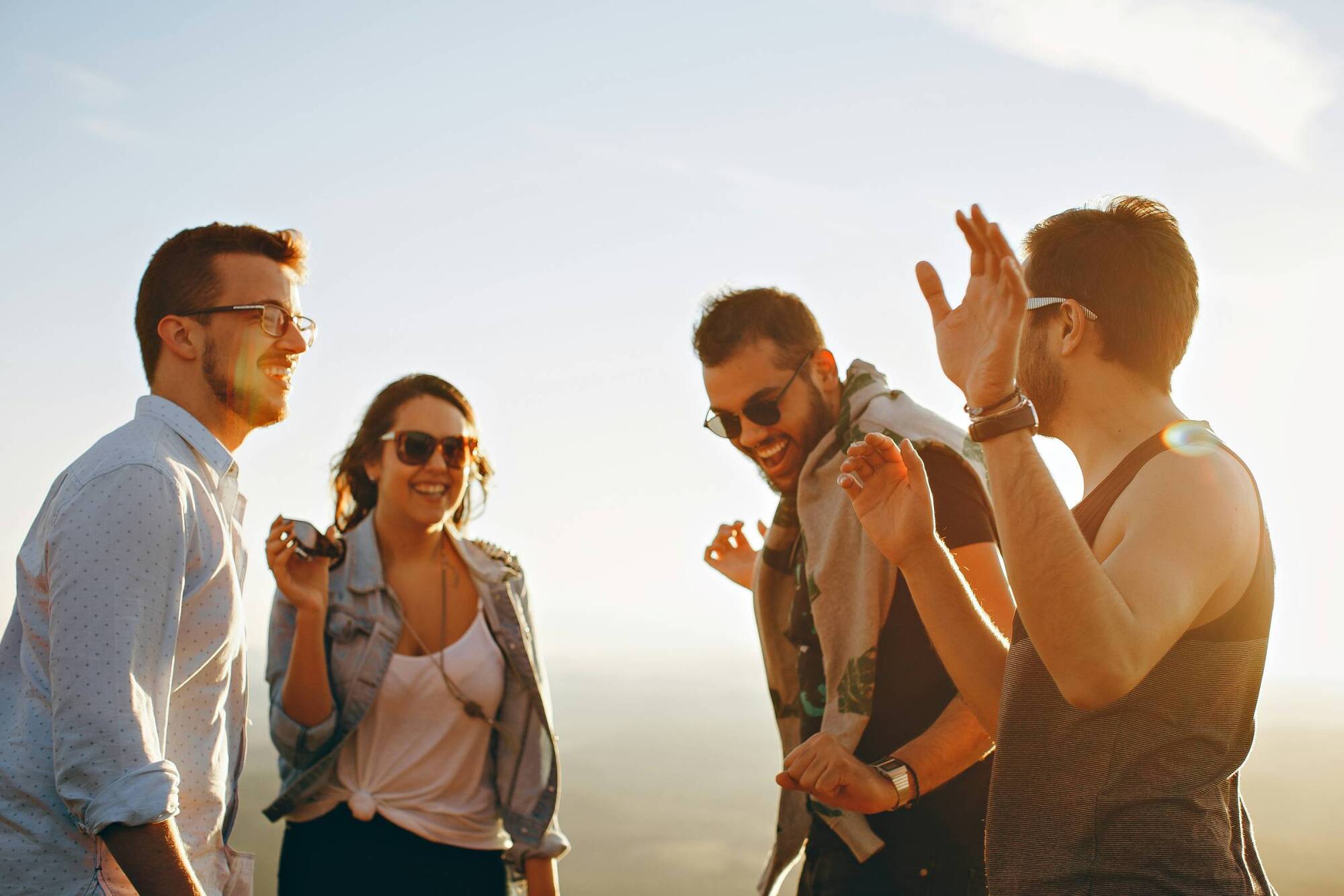 Four friends outdoors laughing and talking together on a sunny day.