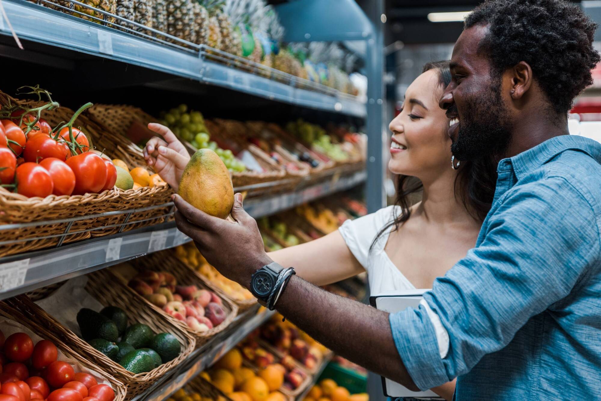 Smiling couple shopping for fresh fruits and vegetables together in a grocery store produce section.