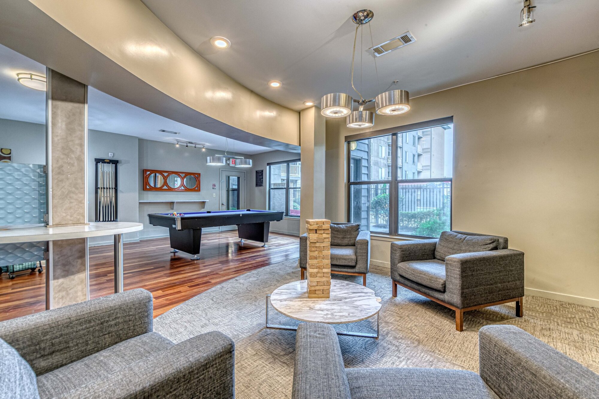Modern lounge at Apex West Midtown with gray chairs, a marble table with Jenga, and a pool table near large windows.