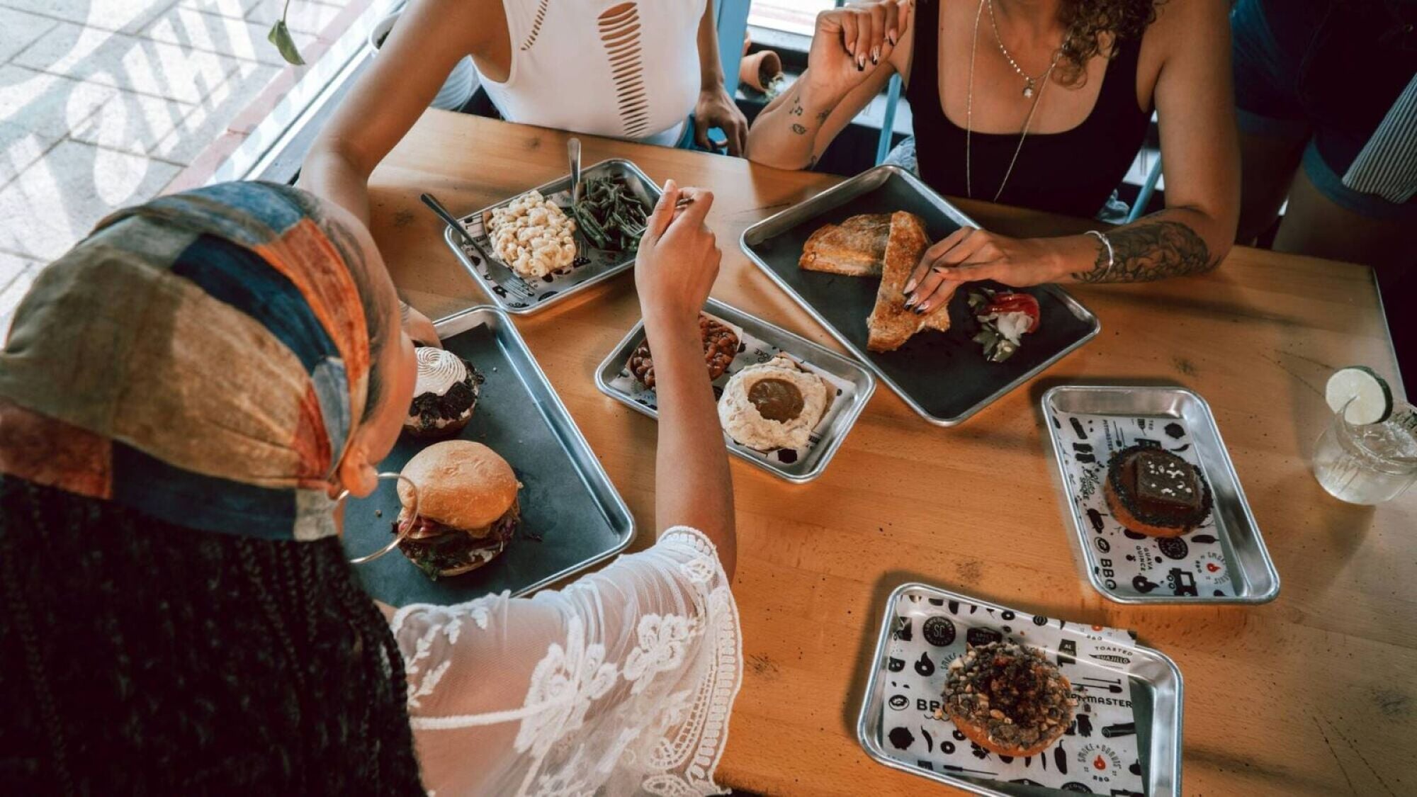 Four people eating assorted meals at a wooden table in a casual restaurant setting, seen from above.