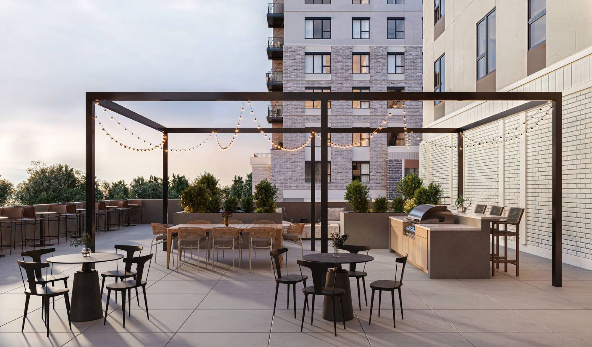 Modern outdoor patio with string lights, dining tables, a grill, and city buildings in the background at Harlow.