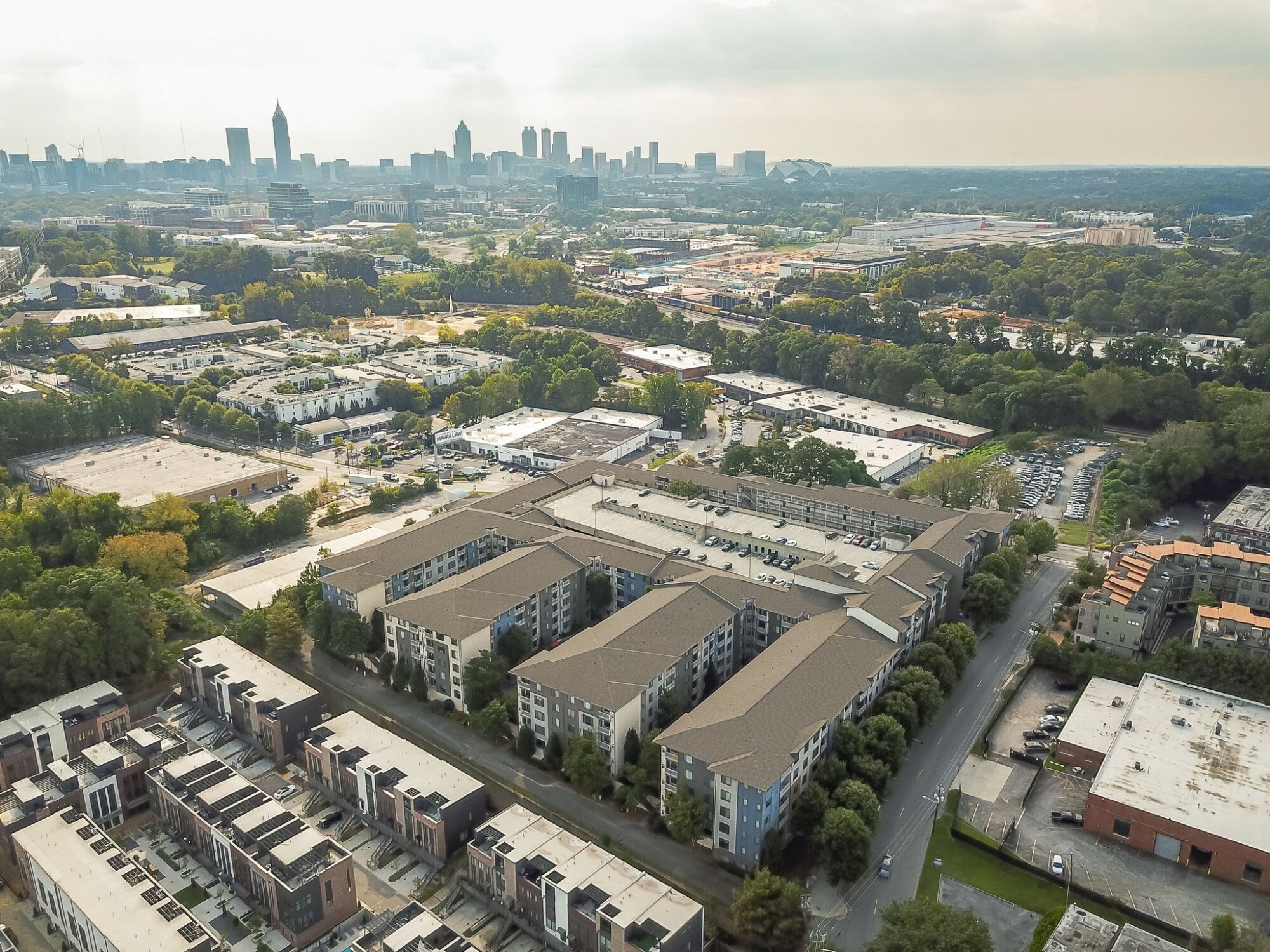 Aerial view of Apex West Midtown apartment buildings with a city skyline in the background on a cloudy day.