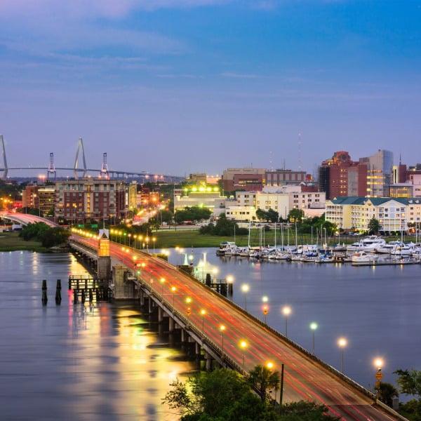 A cityscape at dusk with a bridge and buildings illuminated by streetlights.
