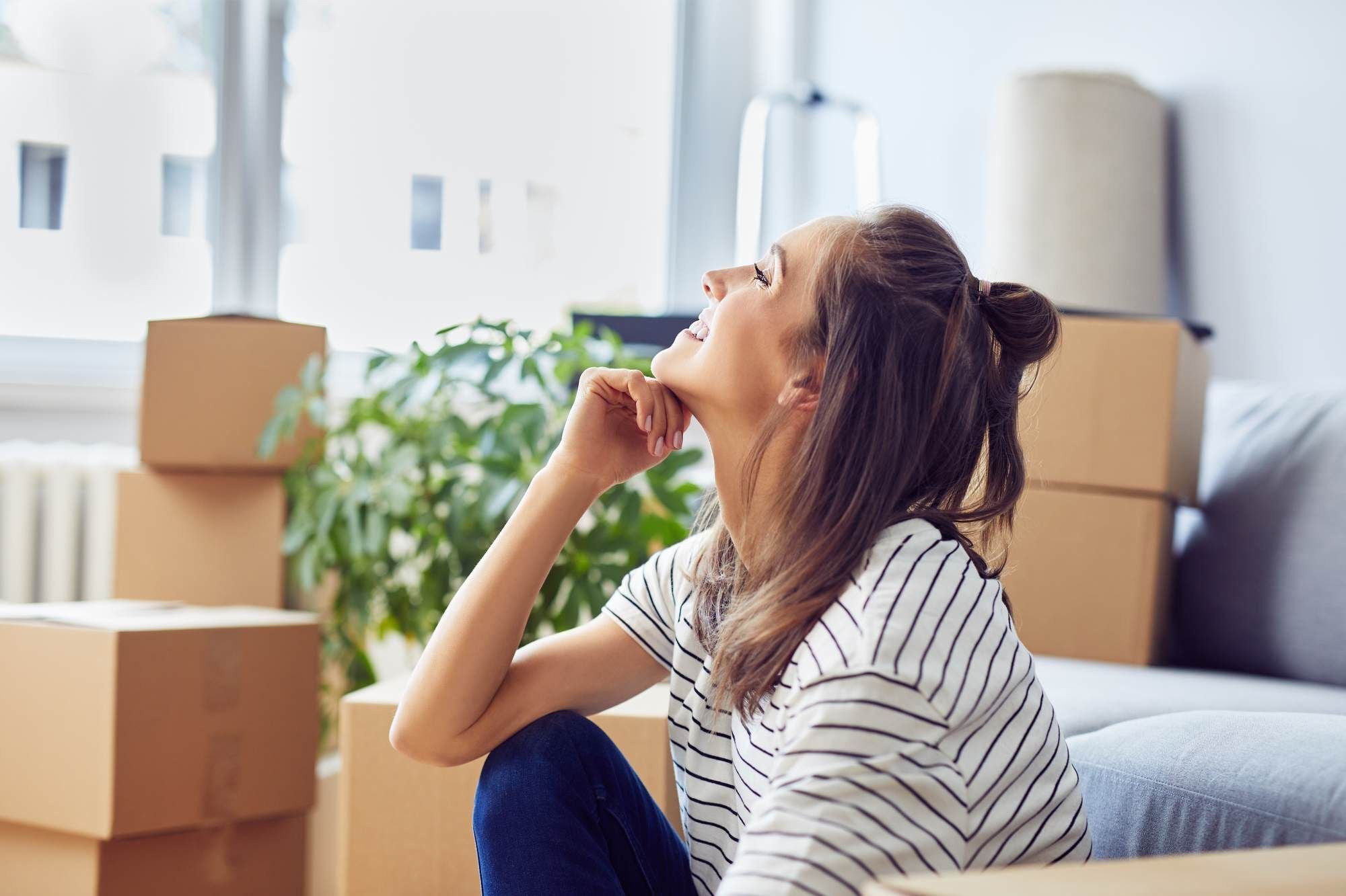 Woman sitting on the floor and smiling, surrounded by moving boxes in a new apartment