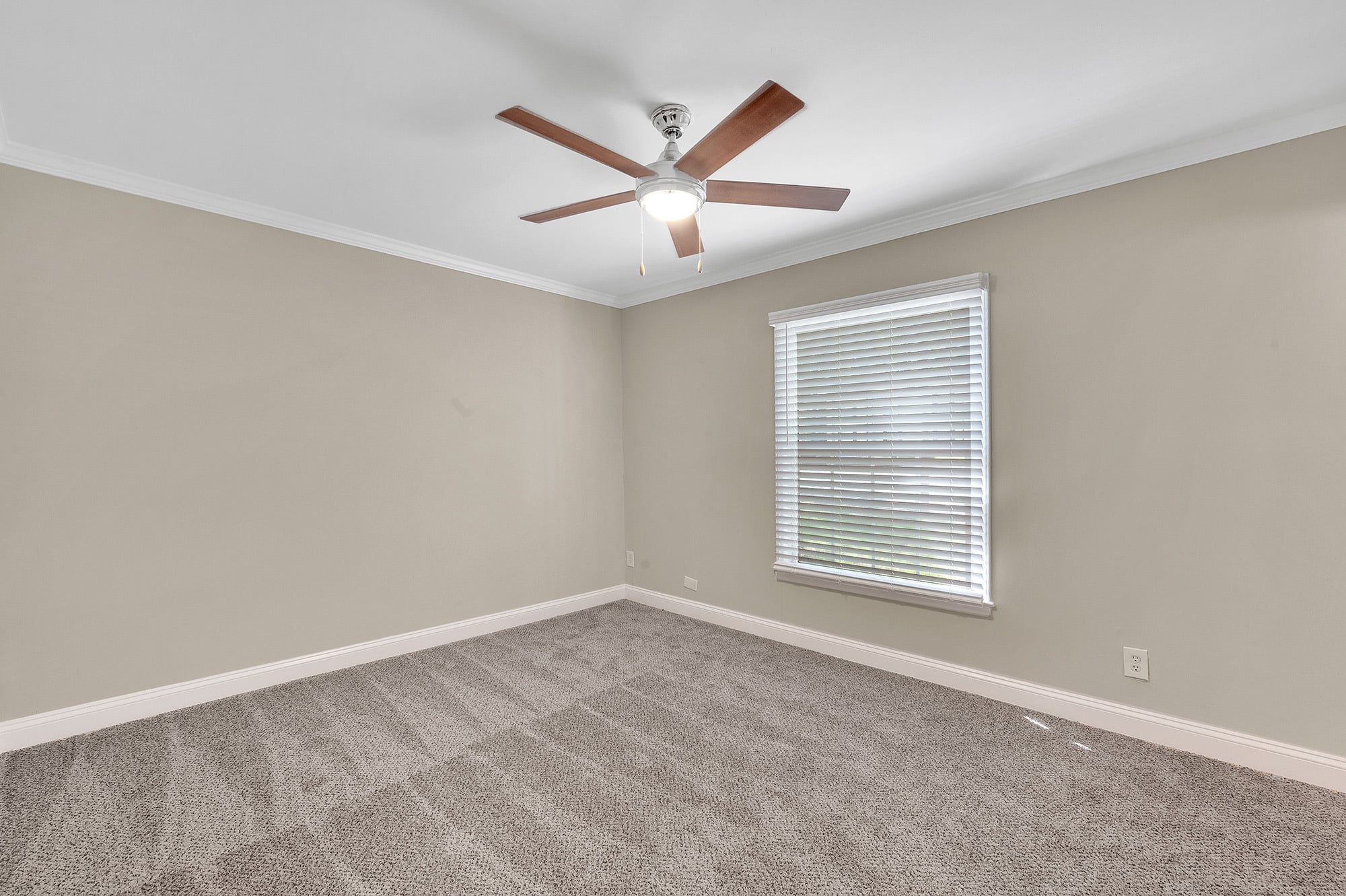 Primary bedroom at Townes at University in Charlotte, NC, with plush carpet, a ceiling fan, crown molding and a wide blinded window.