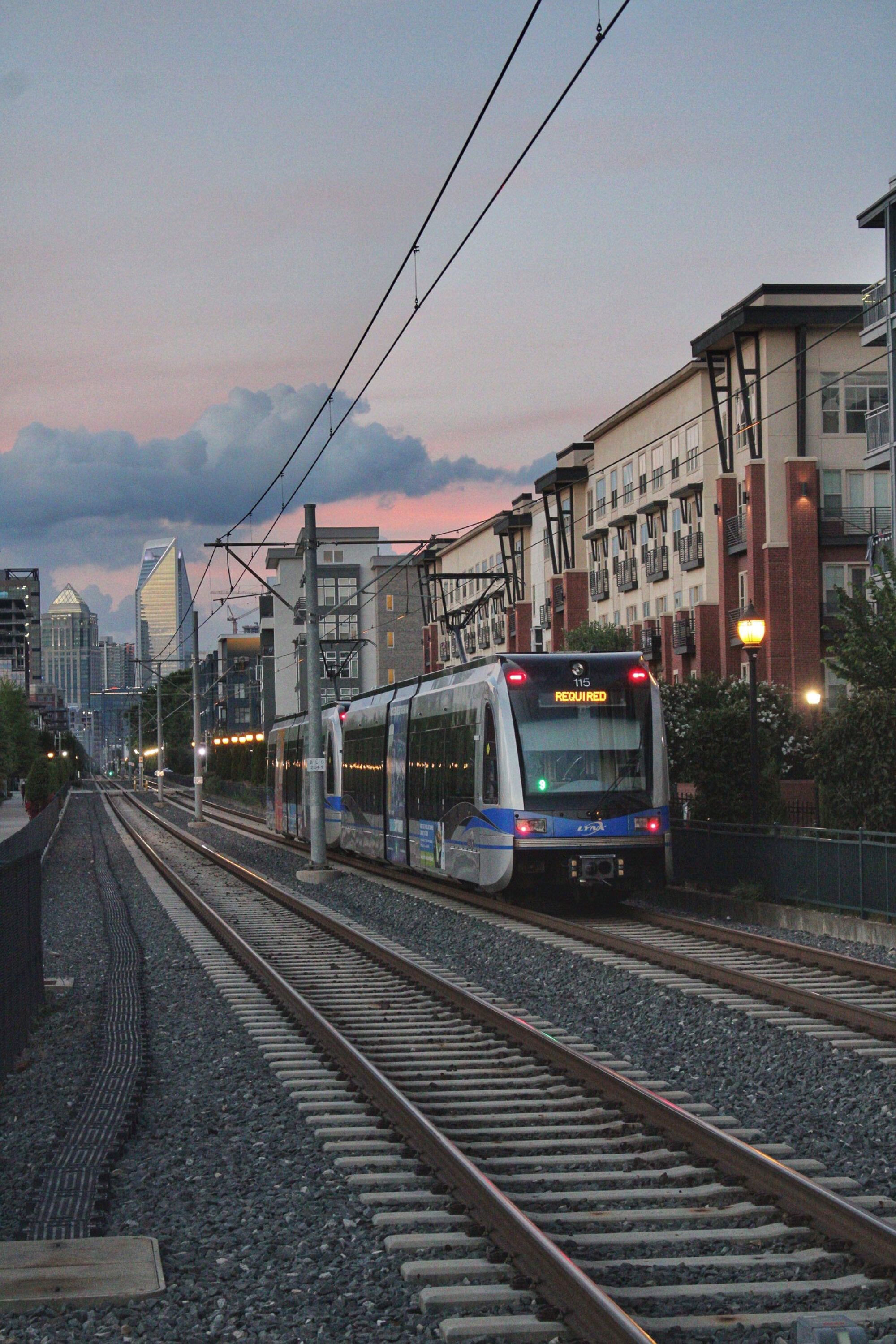 LYNX Blue Line light rail train at dusk with the Charlotte, NC skyline beyond, giving Townes at University residents easy transit access.