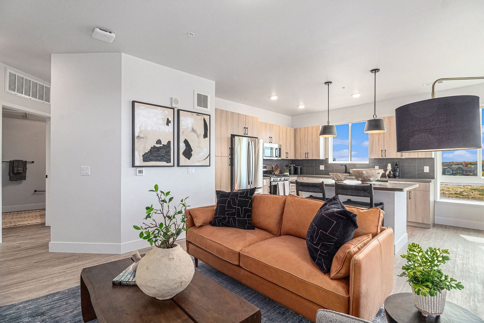 An open-concept living and kitchen area in Solana Central Park with a brown leather couch, abstract wall art, and large windows bringing in natural light.