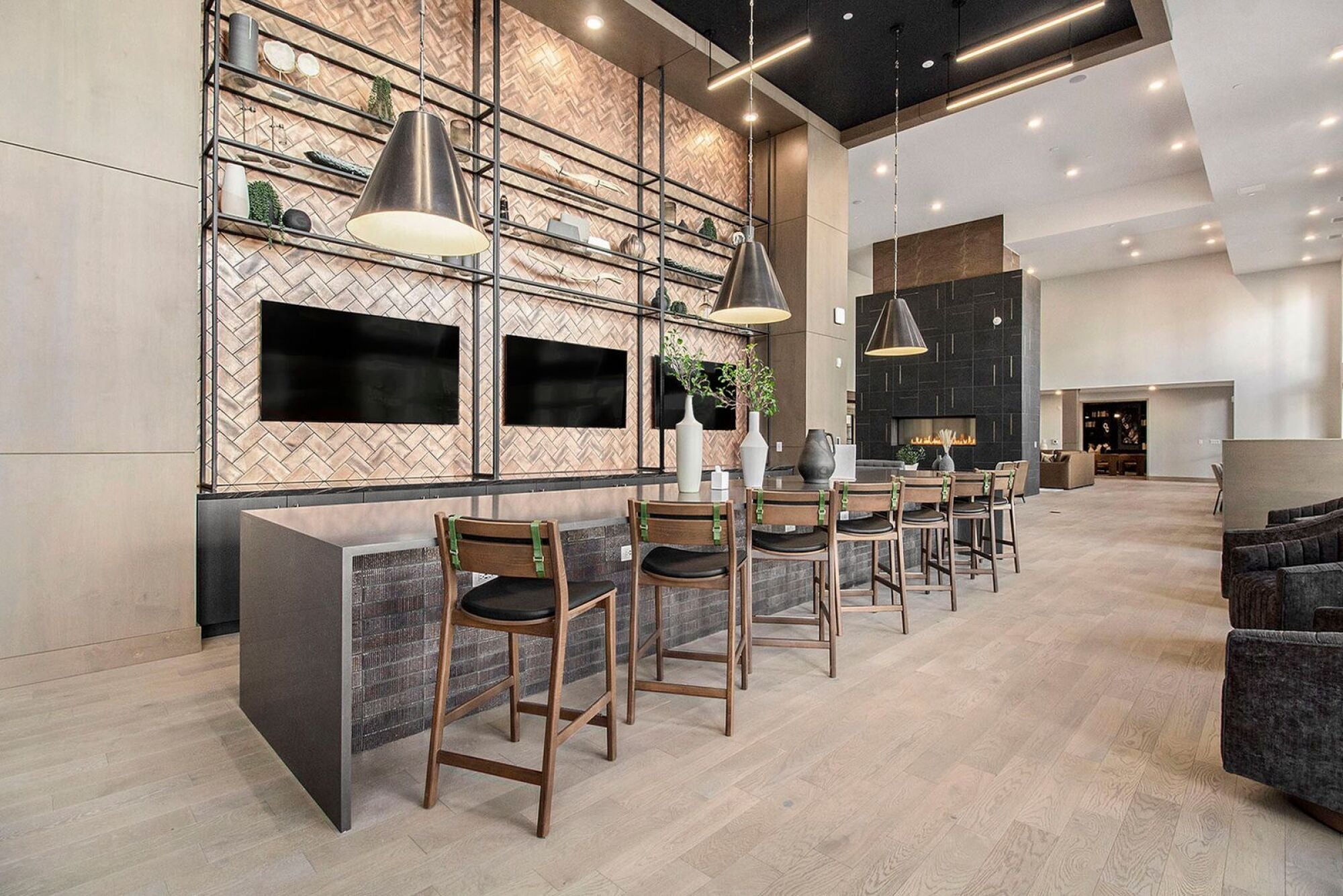 A modern lounge space in Solana Central Park featuring a communal table, wooden high chairs, pendant lighting, and decorative shelving with two large TV screens mounted on the wall.