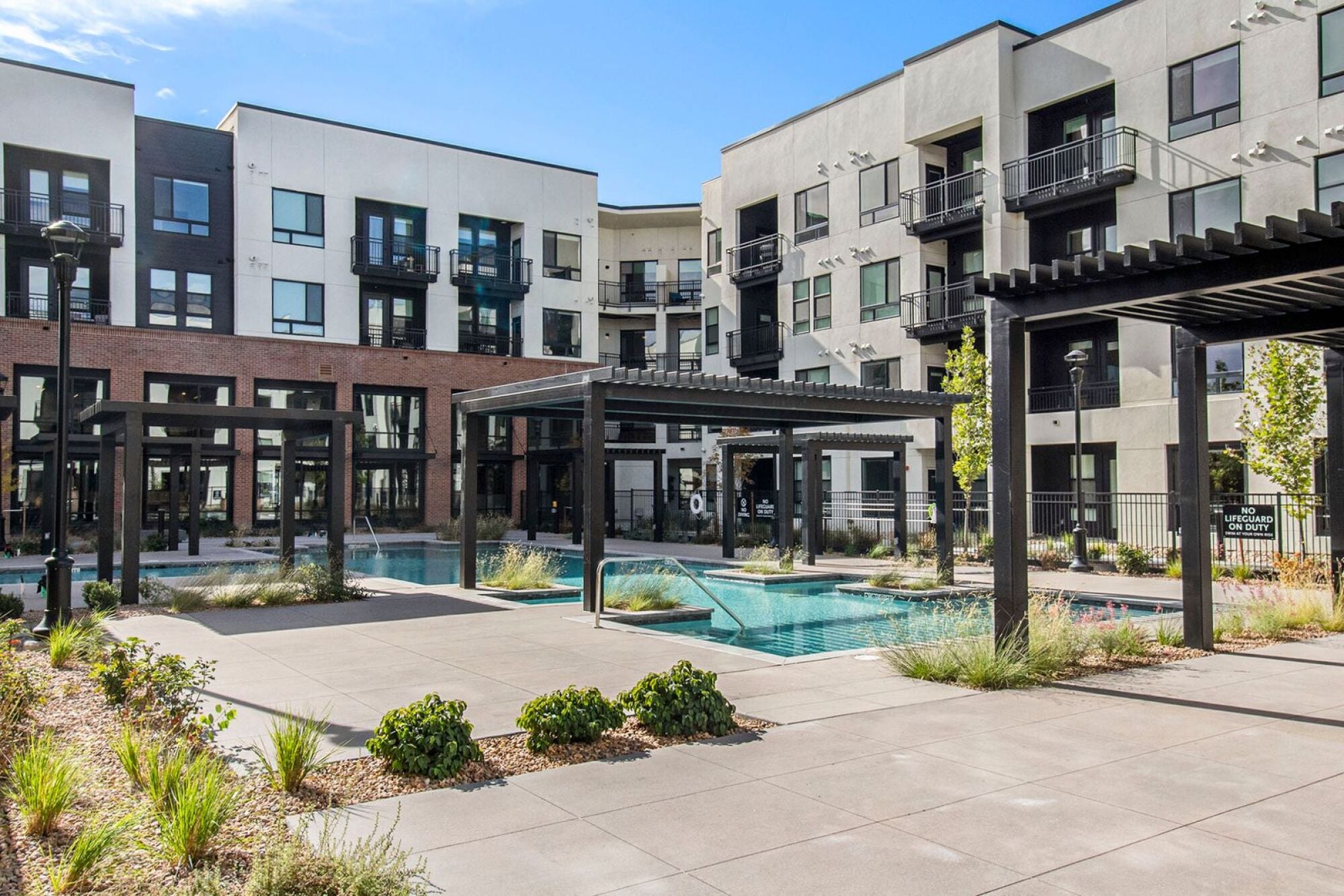 An outdoor view of Solana Central Park's pool area, surrounded by modern apartment buildings with black and white facades and pergolas framing the courtyard.