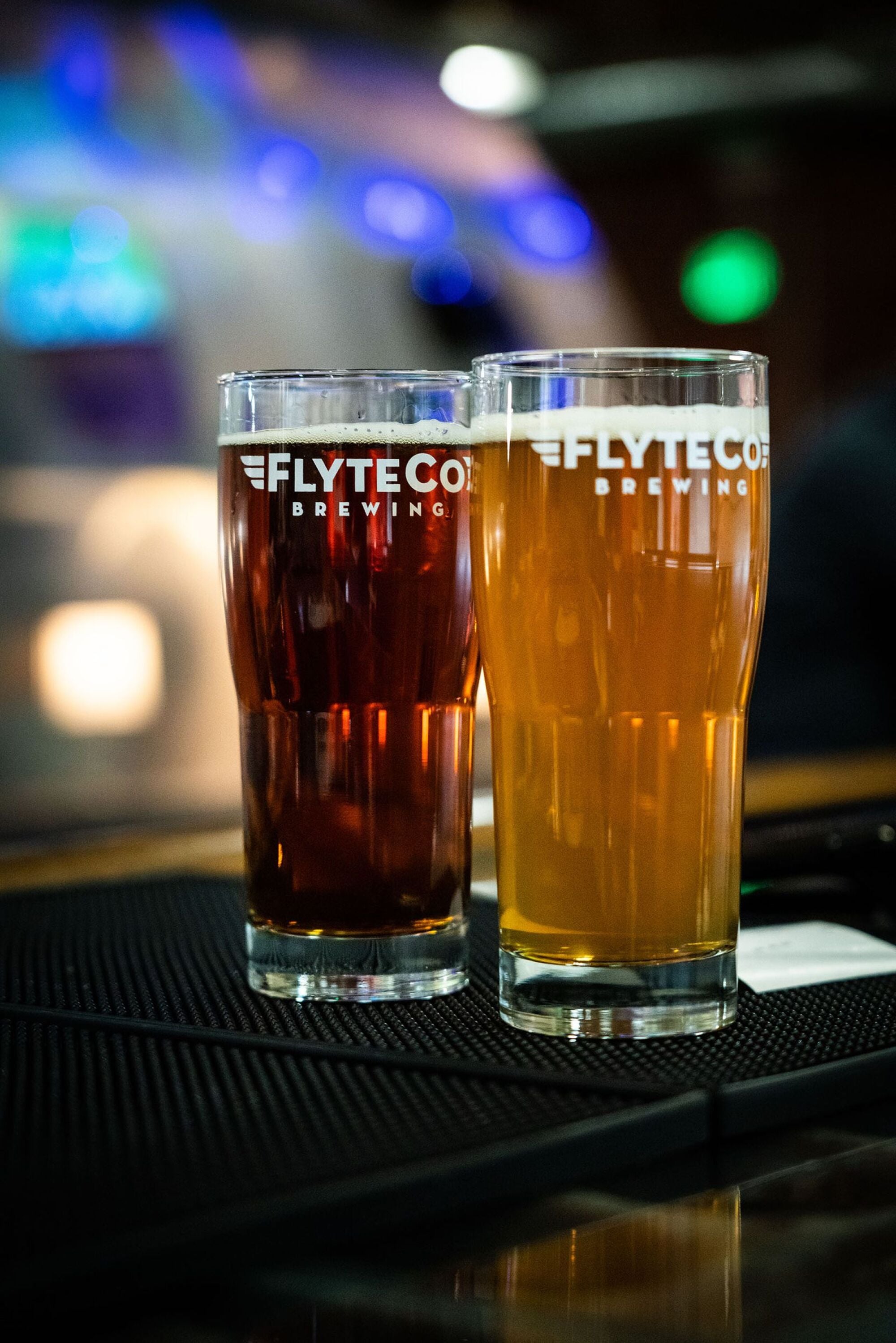 A light beer and a dark beer in pint glasses on a bar countertop