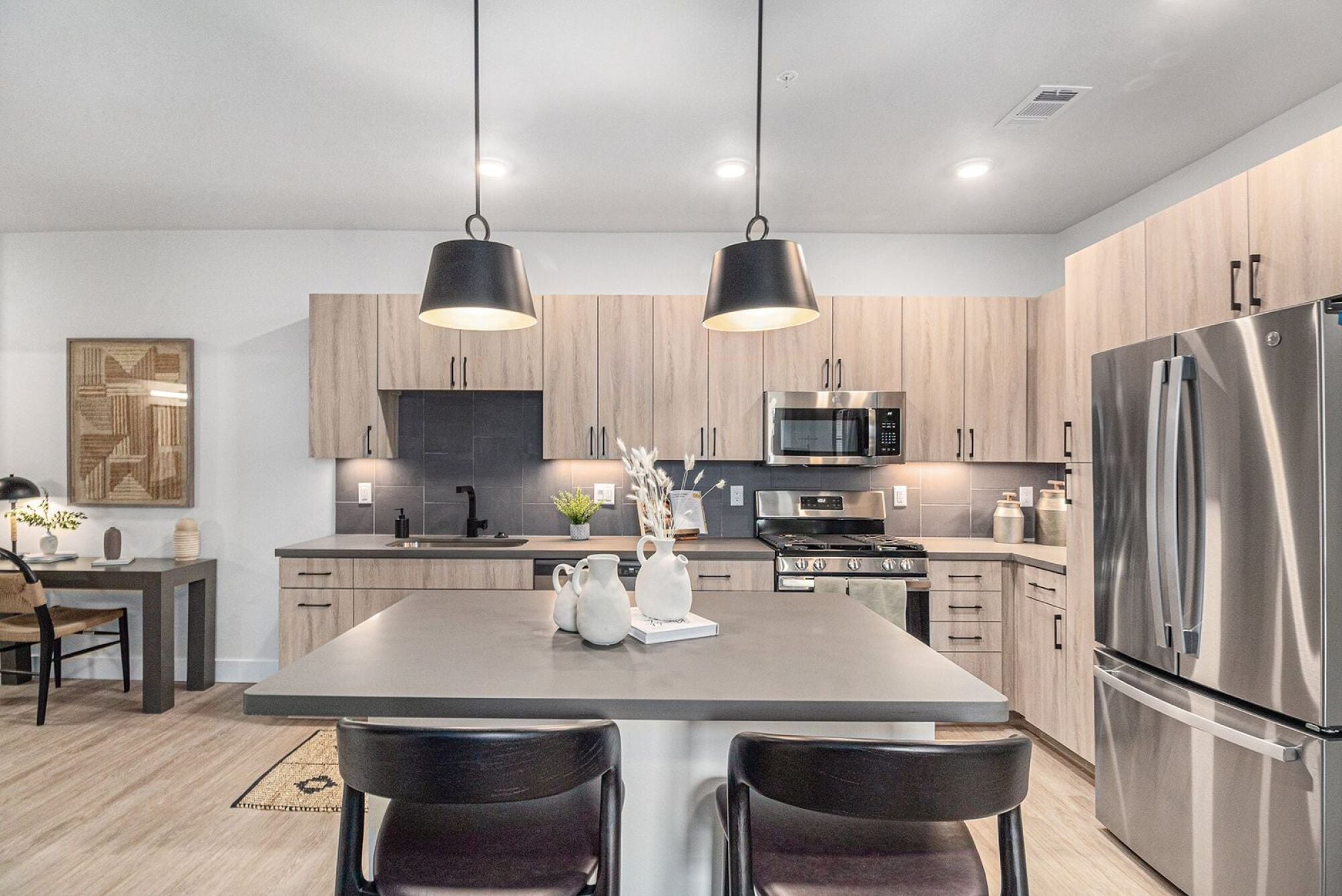 A modern kitchen at Solana Central Park with stainless steel appliances, light wood cabinets, and dark countertops illuminated by pendant lights.