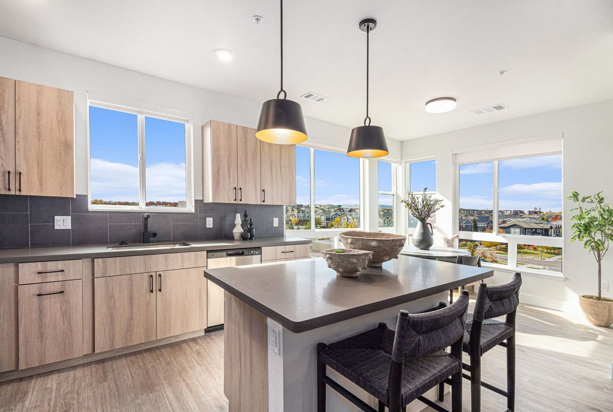 A bright kitchen in Solana Central Park with light wood cabinetry, black countertops, pendant lighting, and views from large windows.