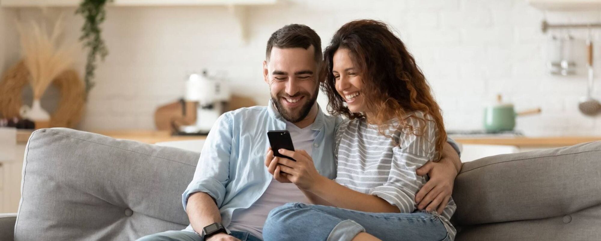 Happy couple looking at cellphone while relaxing on sofa in modern living room