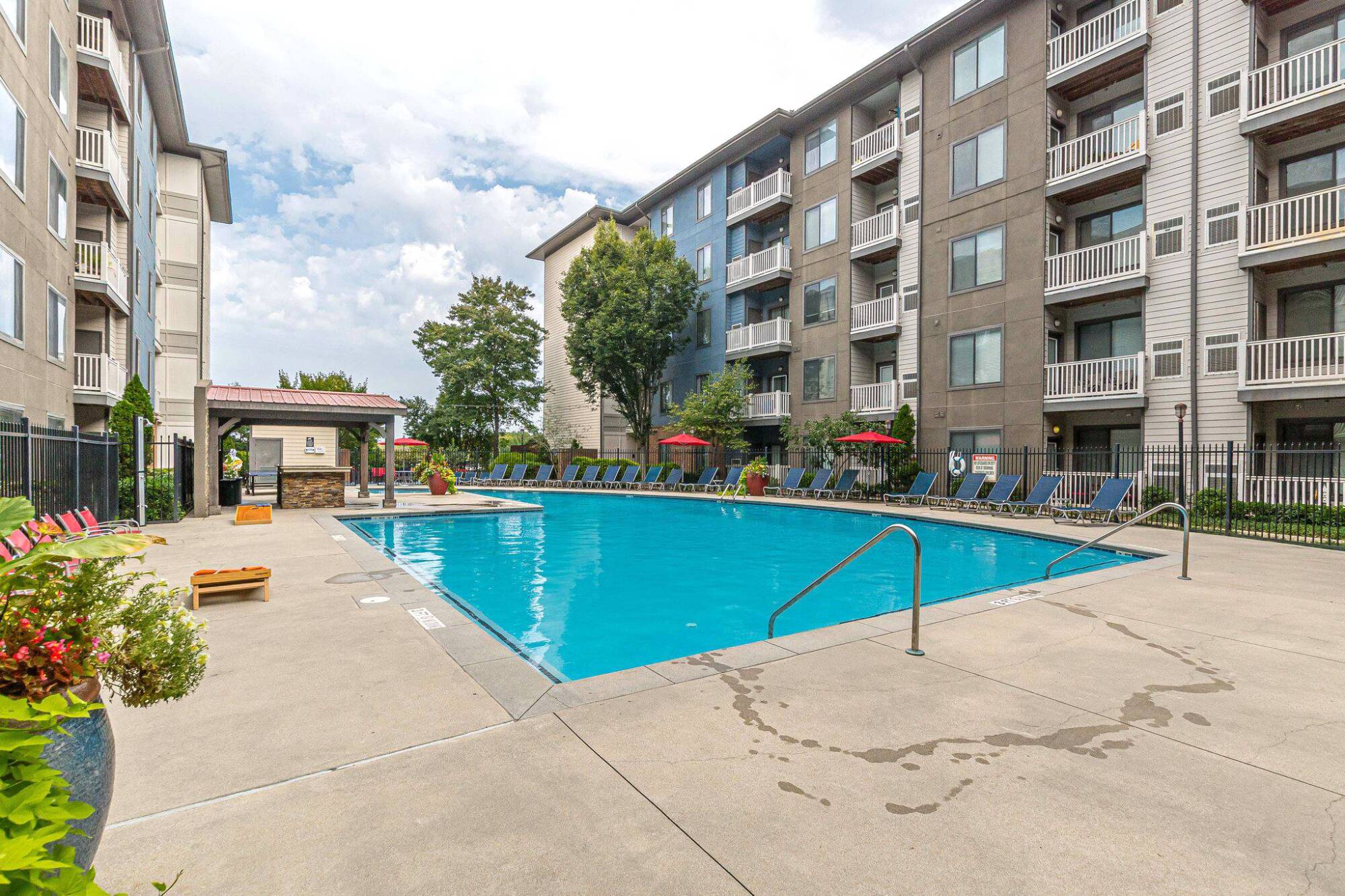 Outdoor apartment pool with lounge chairs, umbrellas, and a covered patio area on a cloudy day at Apex West Midtown.