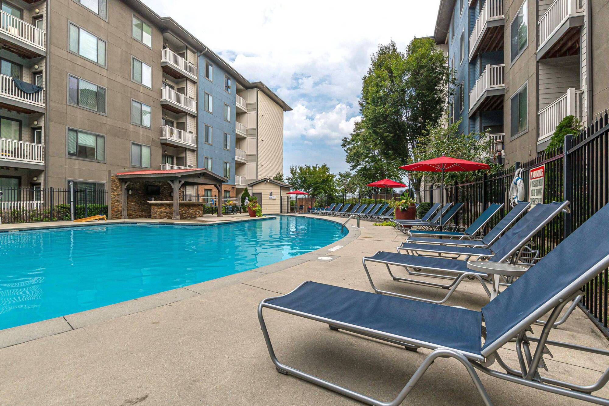 Apartment pool area with blue lounge chairs, red umbrellas, and surrounding multi-story buildings at Apex West Midtown.