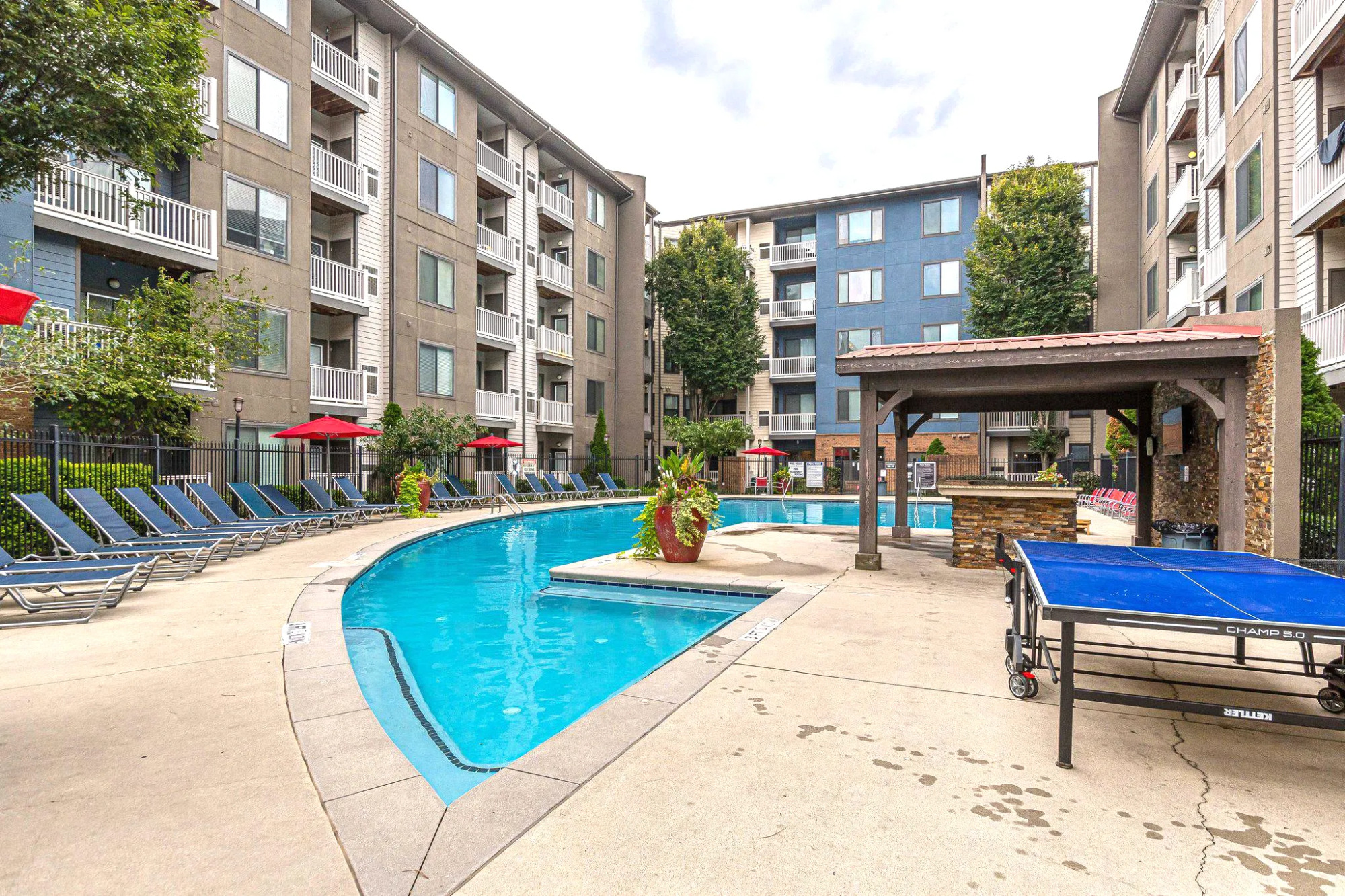 Outdoor apartment pool area with lounge chairs, a pergola, and a blue ping pong table near the water at Apex West Midtown.