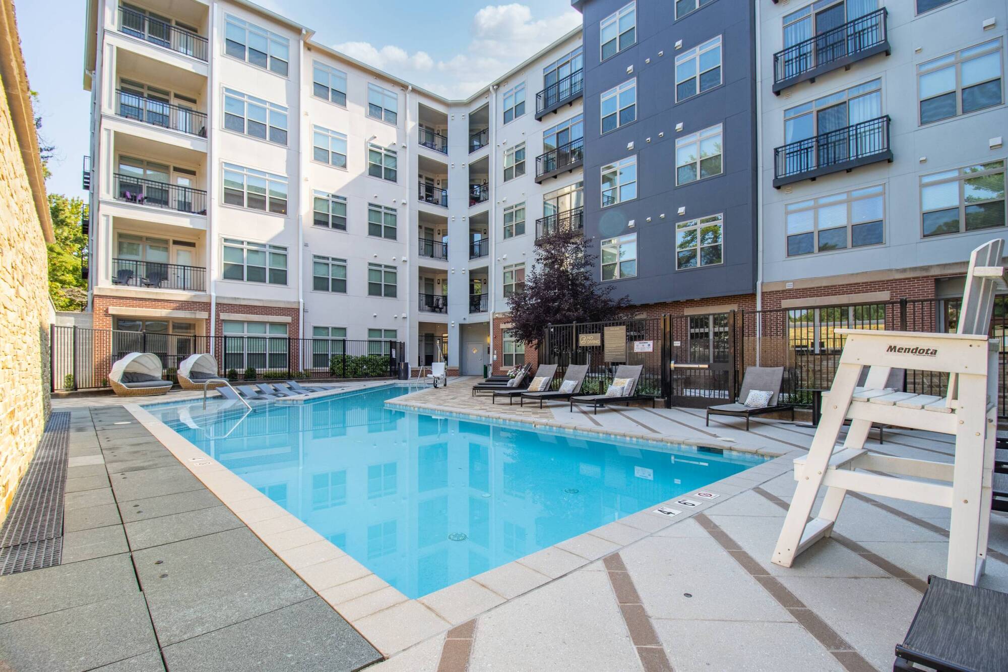 Milestone Apartments Outdoor patio with Adirondack chairs around a fire pit, surrounded by trees and apartment buildings.