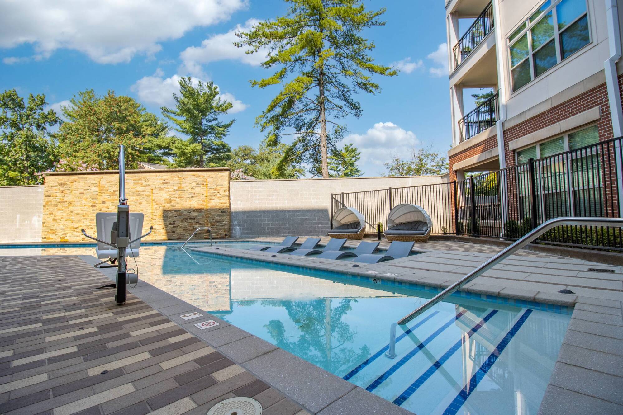 Milestone Apartments Wood pergola with picnic tables and grills in a sunny outdoor apartment courtyard surrounded by trees.