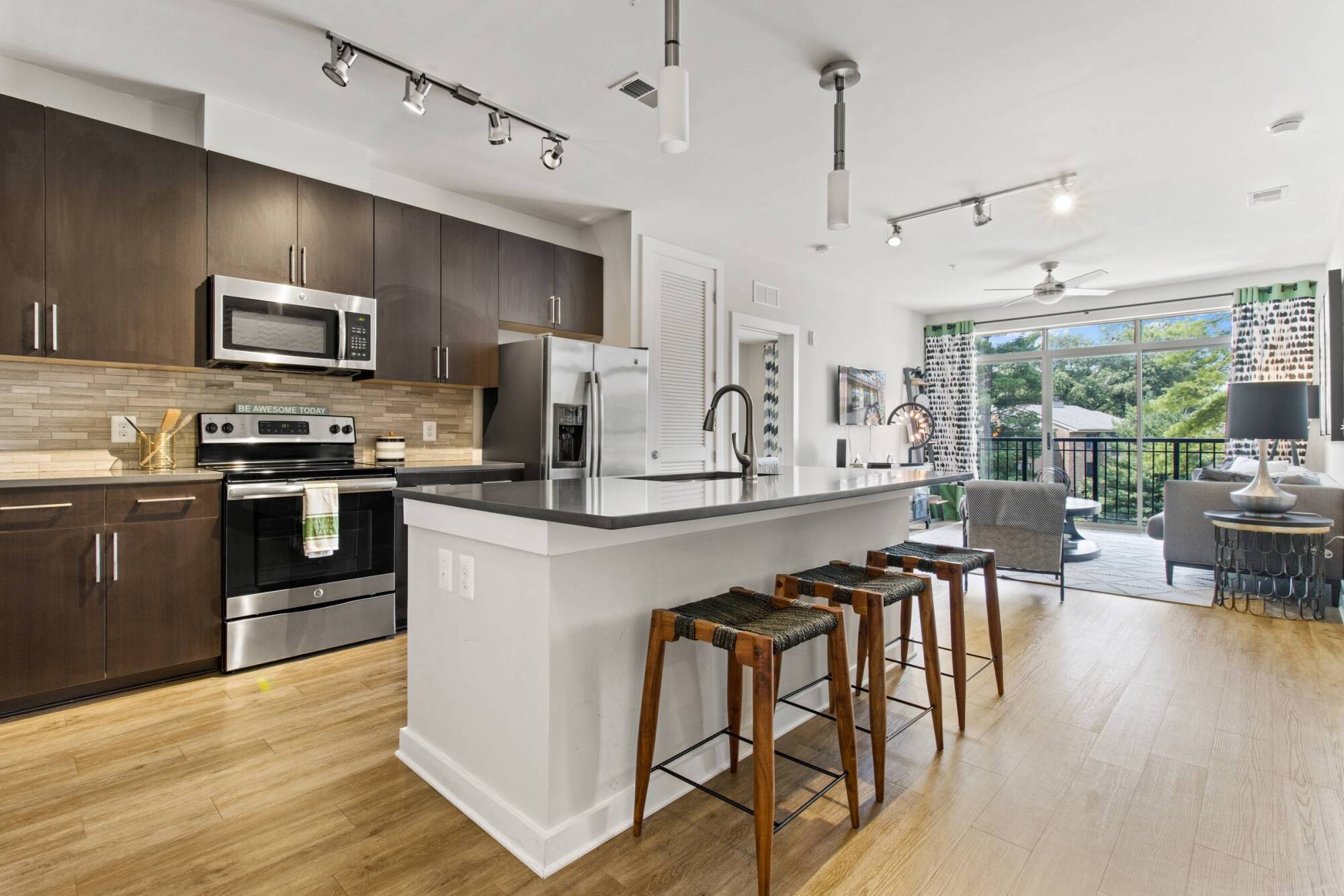 Milestone Apartments Modern kitchen with white cabinets, stainless steel appliances, and a marble island set for two.